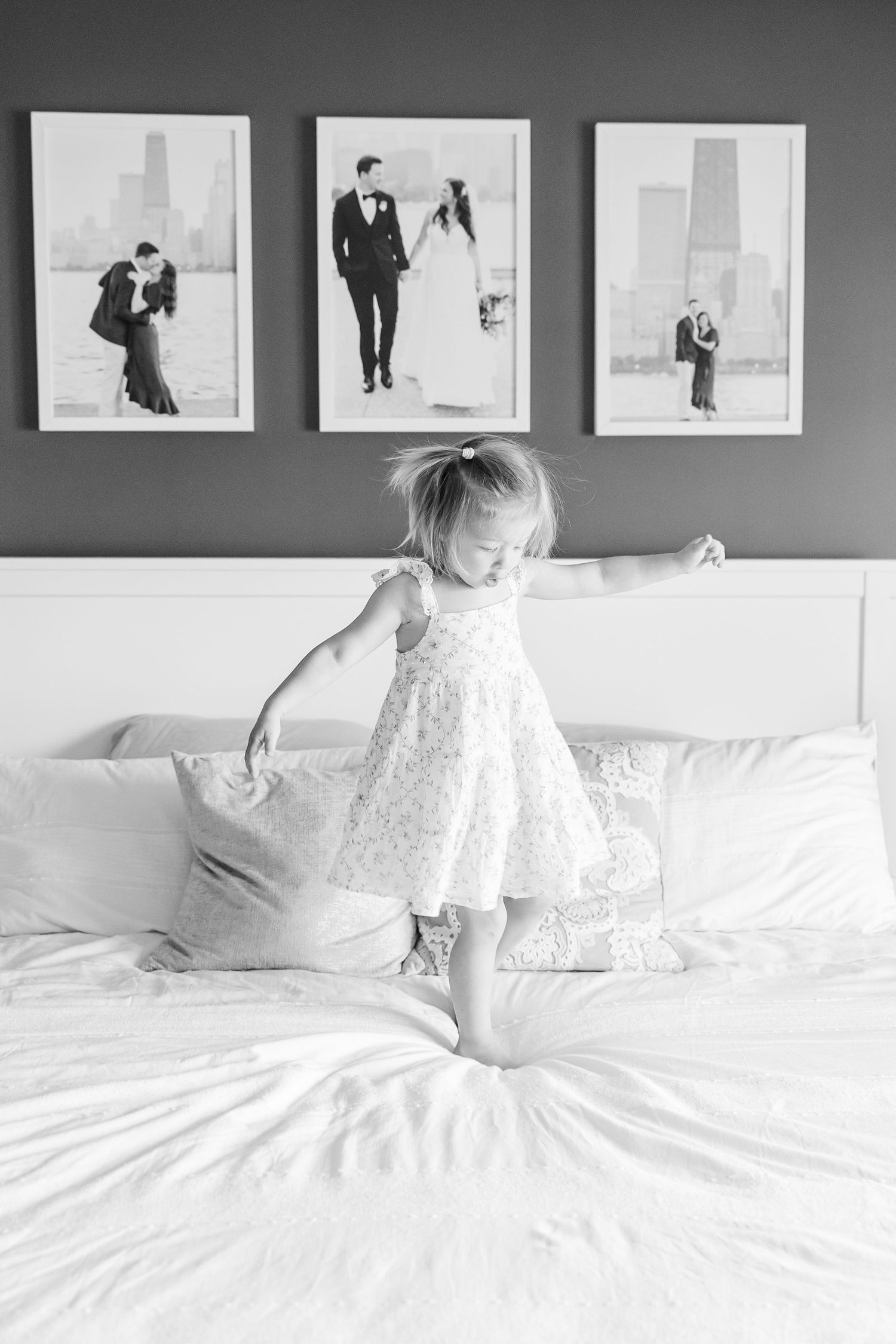 Black and white photo of big sister dancing on the bed during an in-home lifestyle newborn session