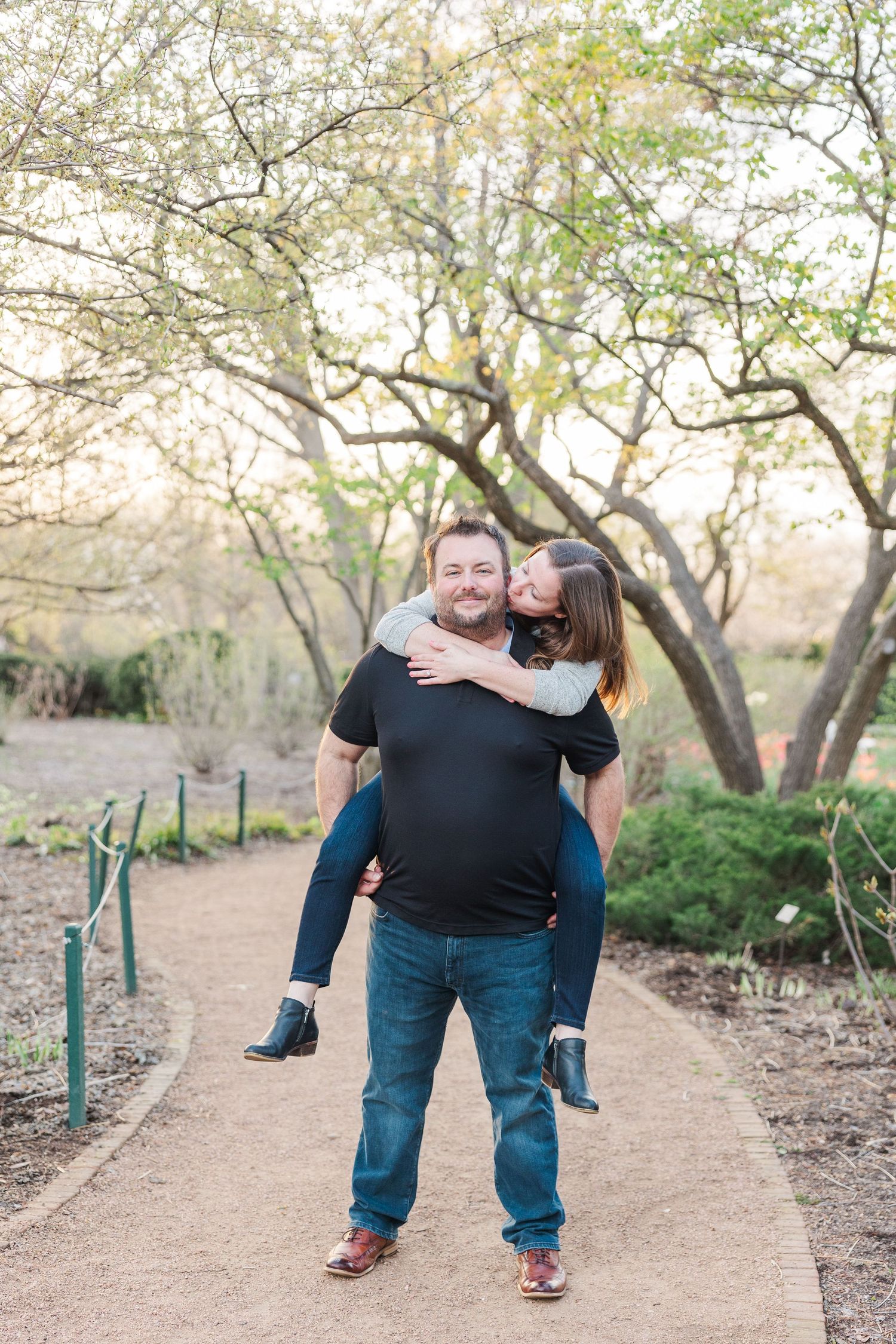 Playful piggyback ride on garden path surrounded by trees.