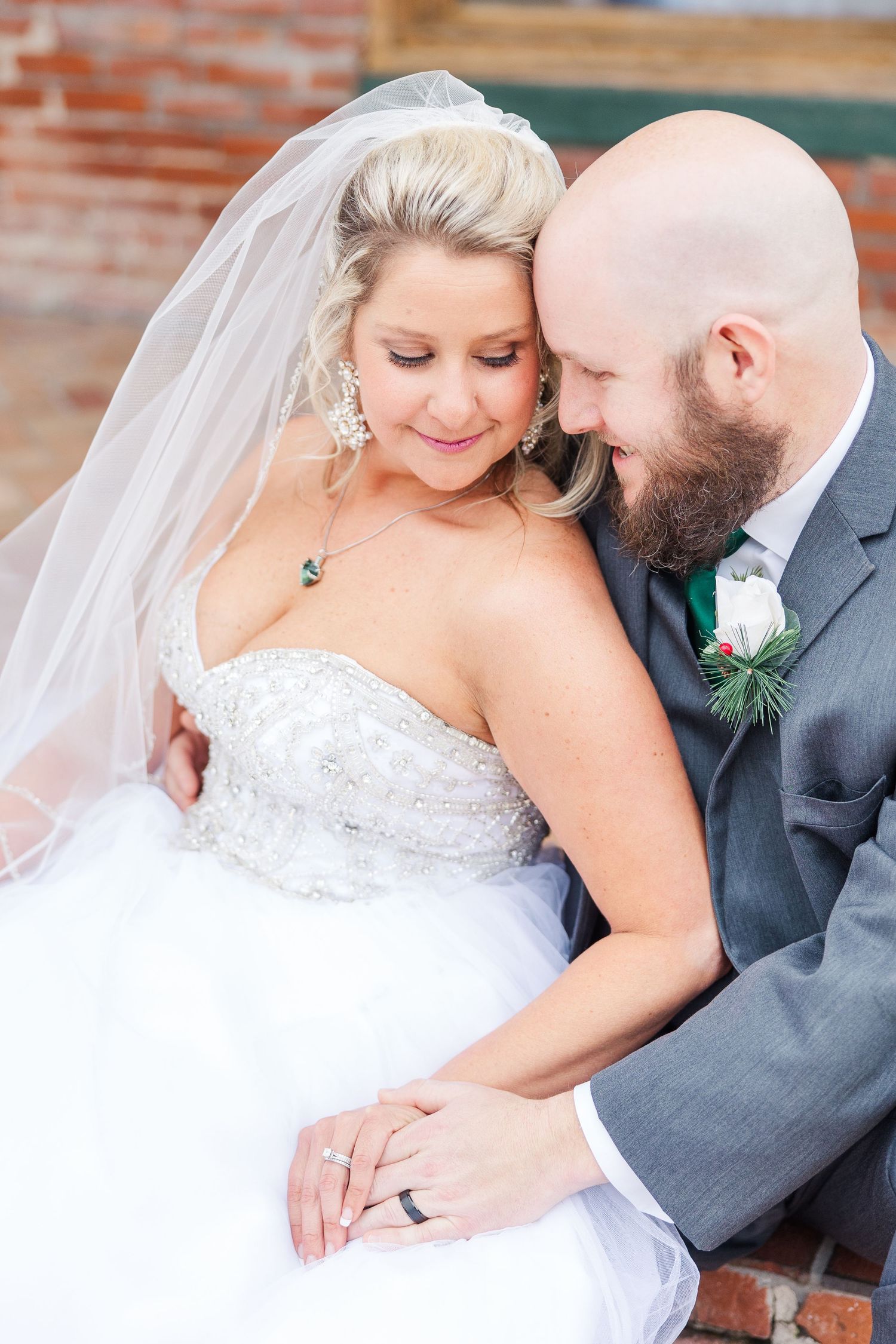 Intimate wedding portrait showing tender moment between couple against brick backdrop.