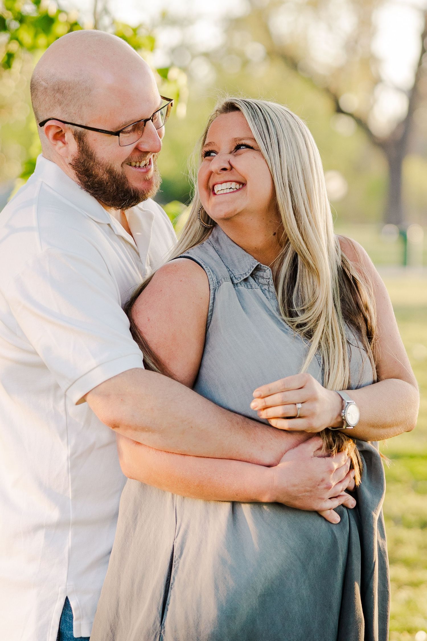 A romantic couple embraces outdoors in warm sunlight while sharing joyful laughter together.