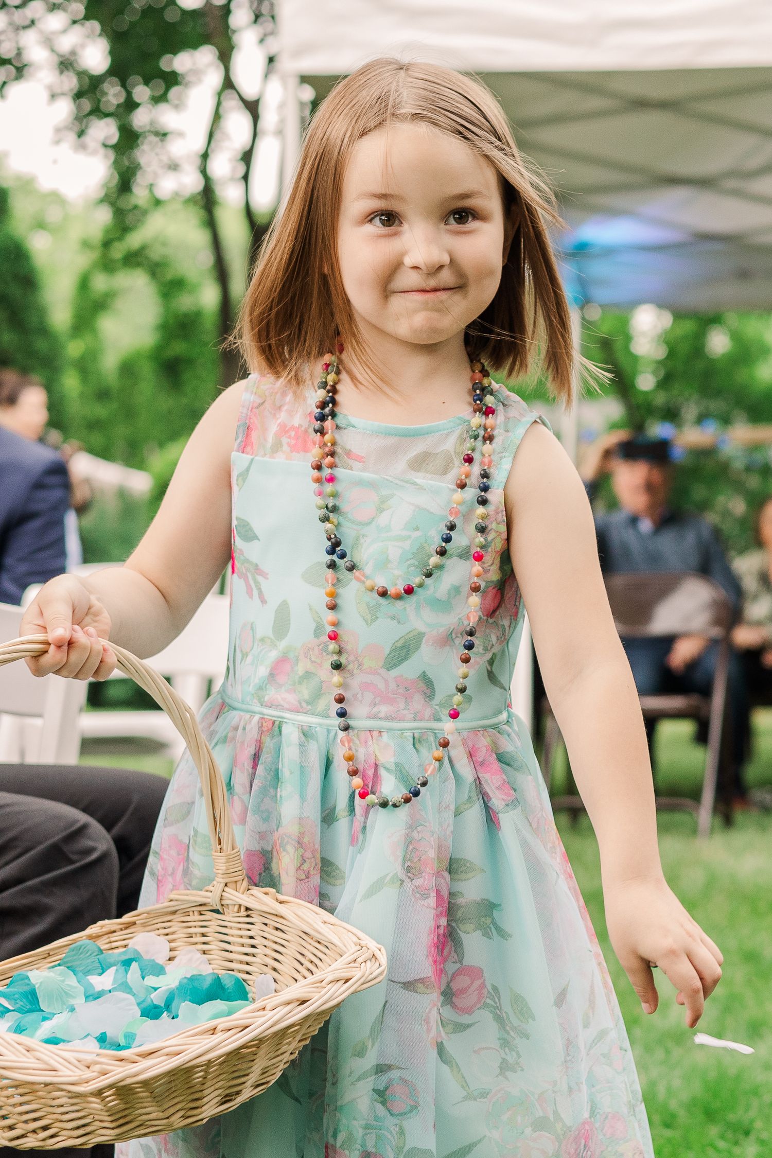 Young girl in floral dress carries basket at outdoor summer celebration.
