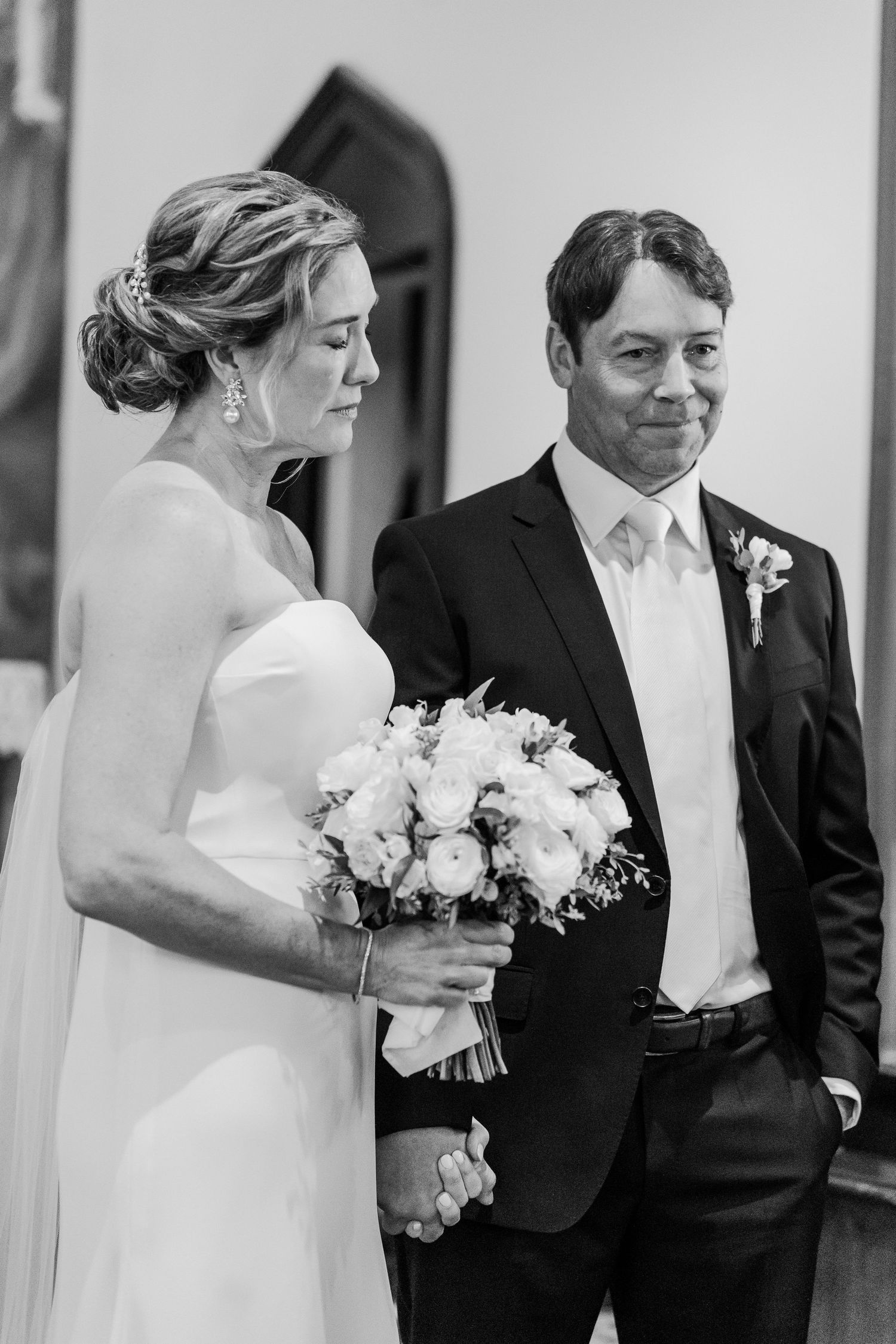 A classic black and white portrait of a couple in formal wedding attire holding a white floral bouquet.