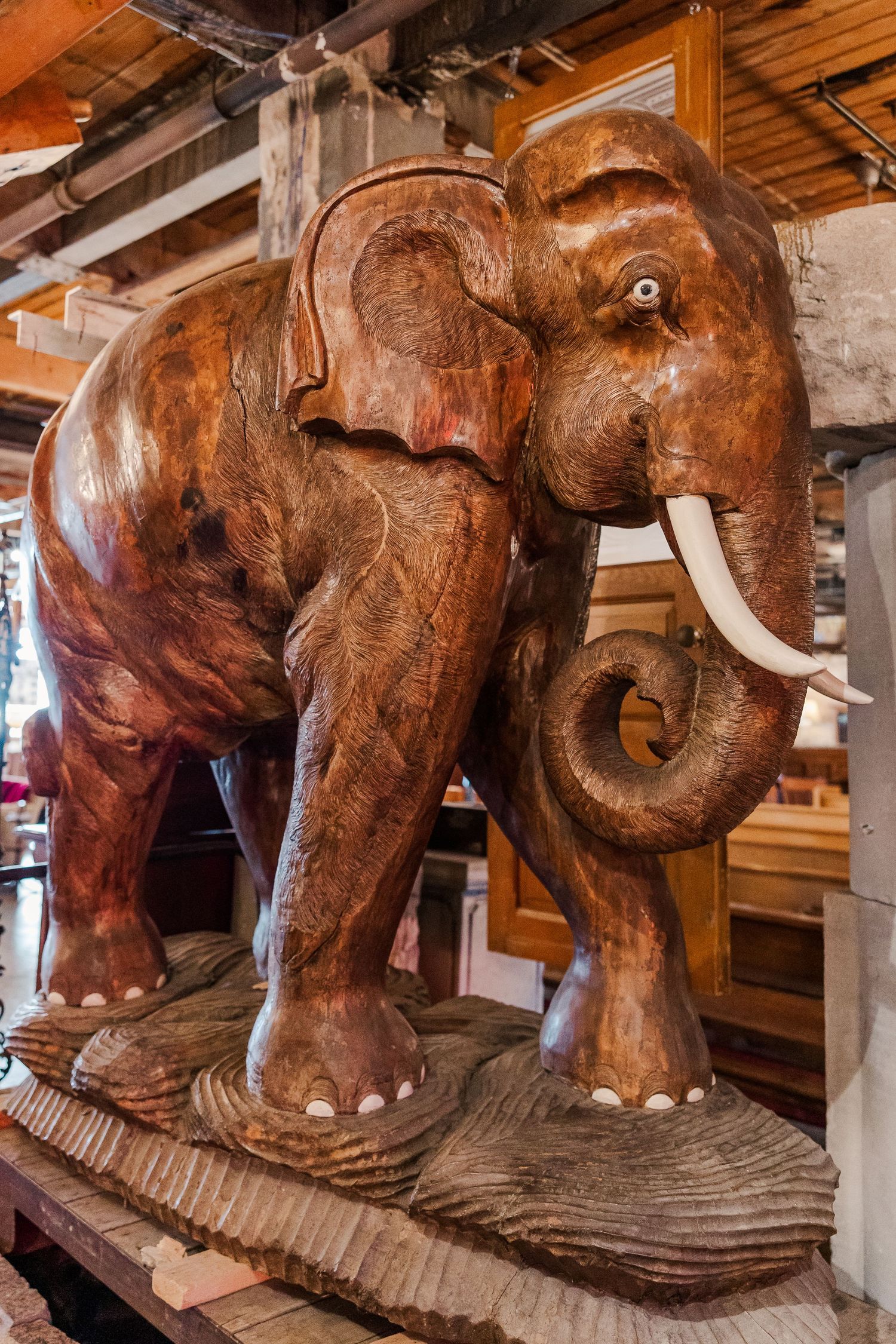 Large carved wooden elephant statue with detailed tusks and textured surface displayed on wooden platform.