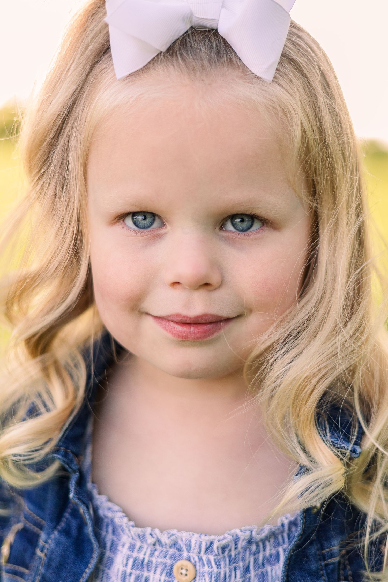 Portrait with a white bow accessory and blue dress against a soft focus nature background.