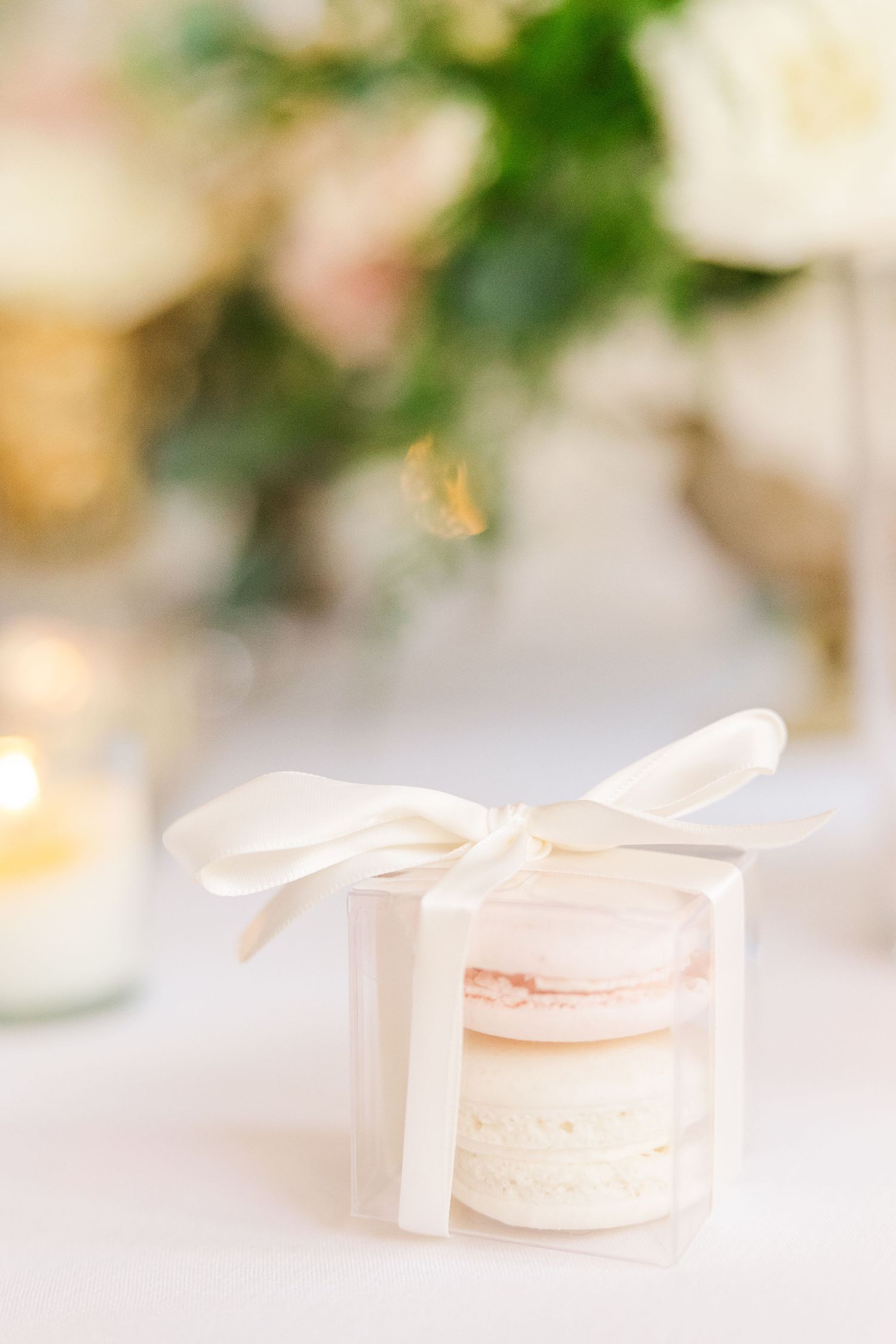 White gift box tied with ribbon containing pale pink and white macarons.