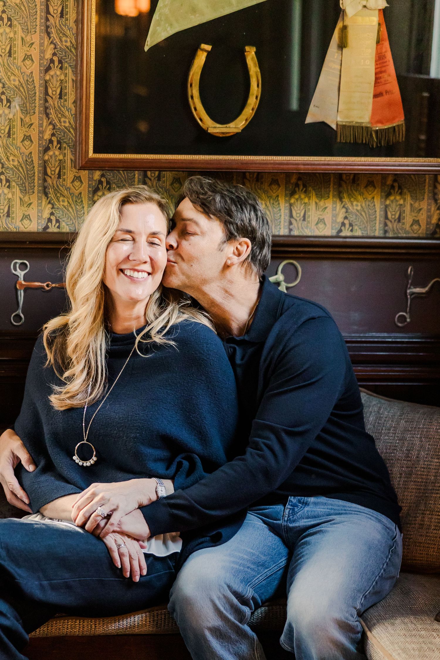 A romantic moment captured on a vintage couch with decorative horseshoe art in background.