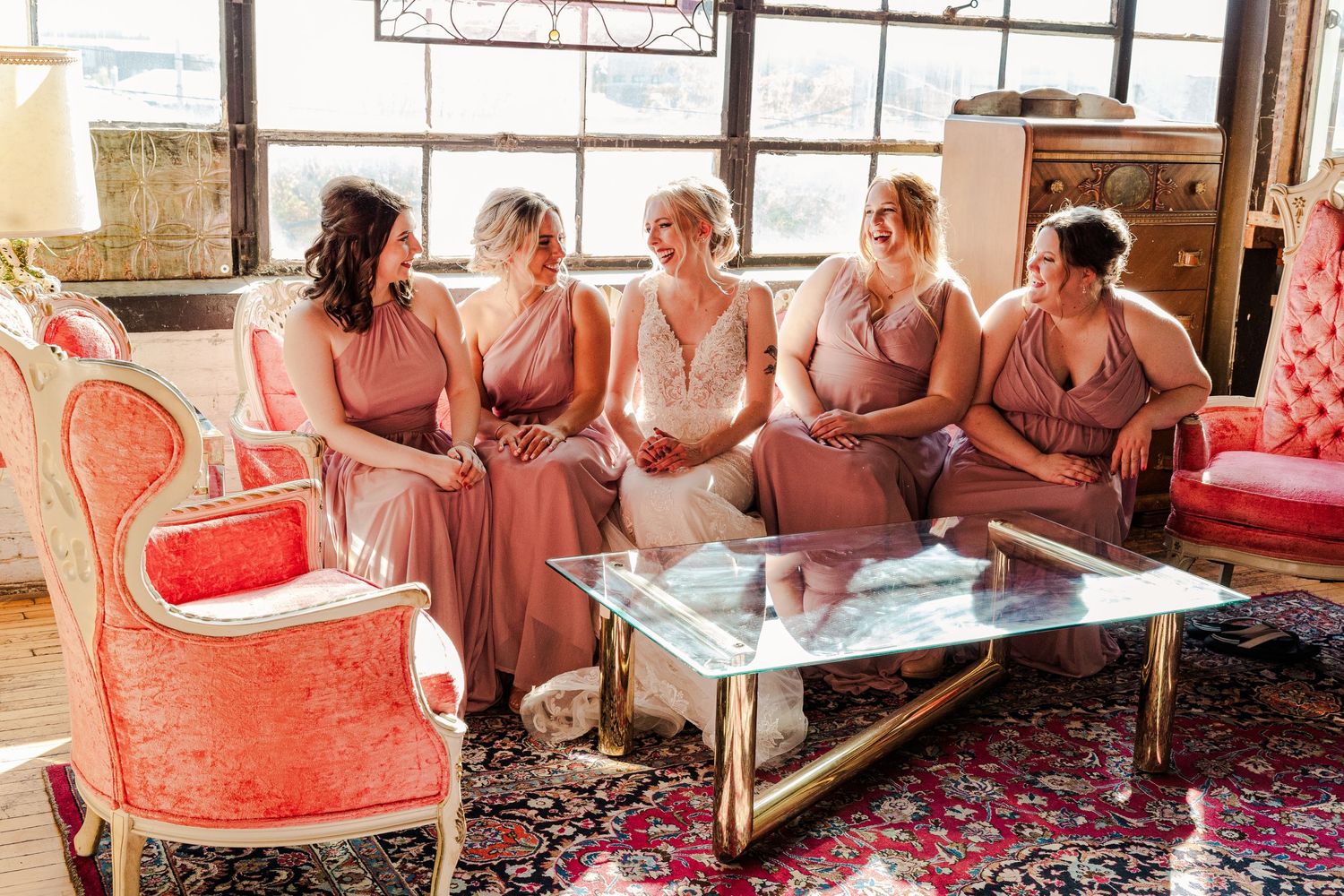 Wedding party relaxing on vintage furniture in coordinated pink dresses.