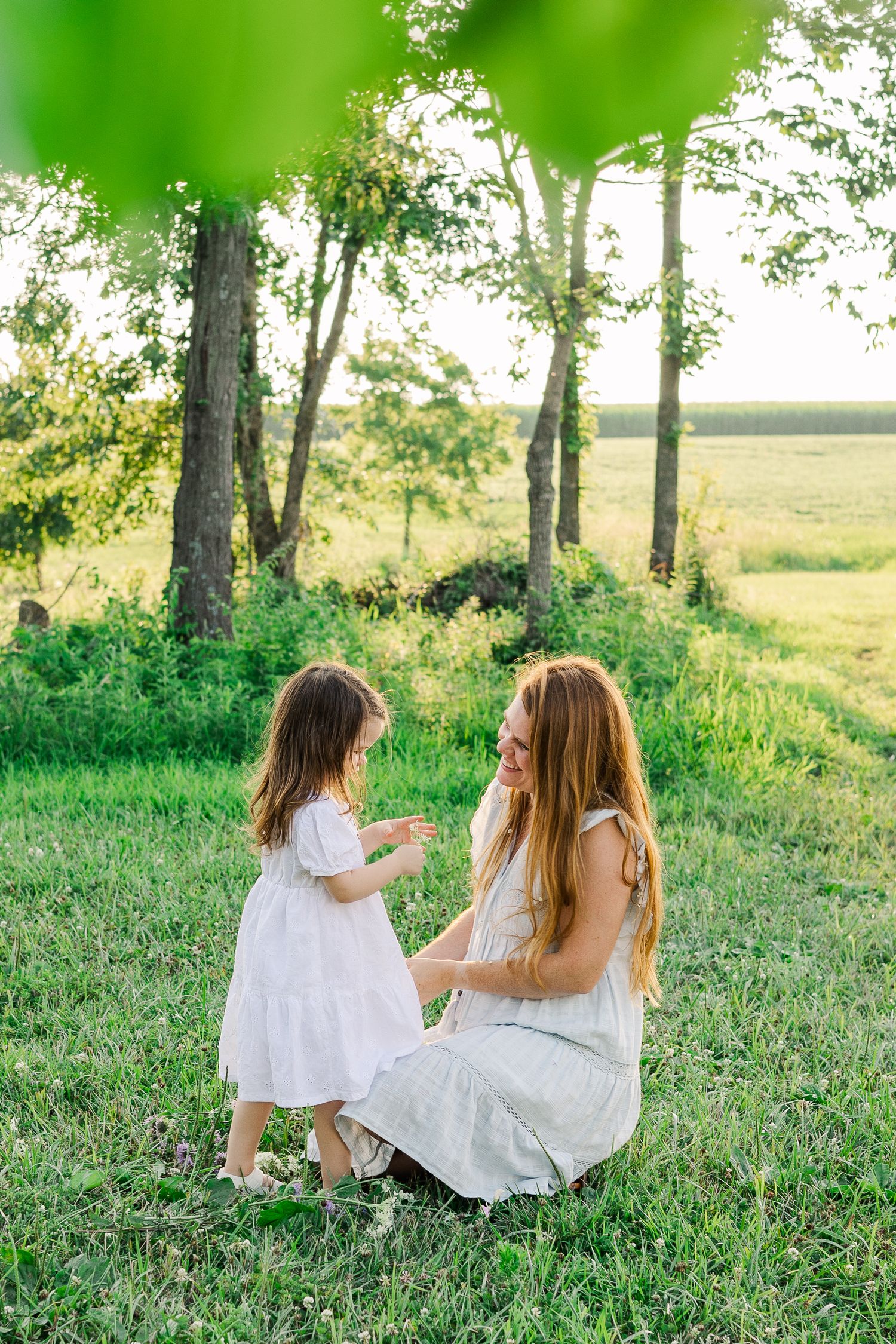 Two people in white dresses sharing an intimate conversation in a sunlit field.