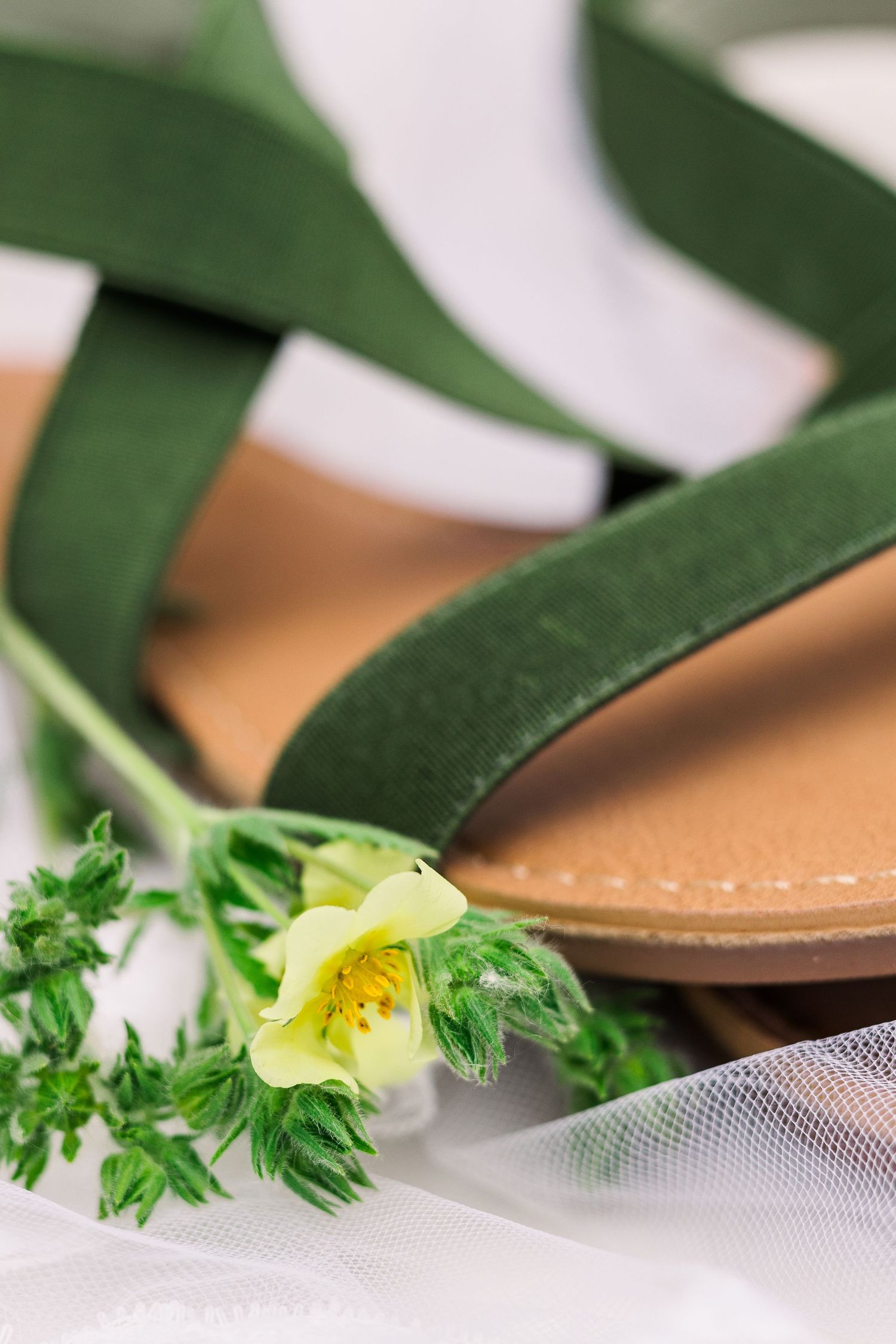 Green sandal with delicate white flower detail against white tulle background.