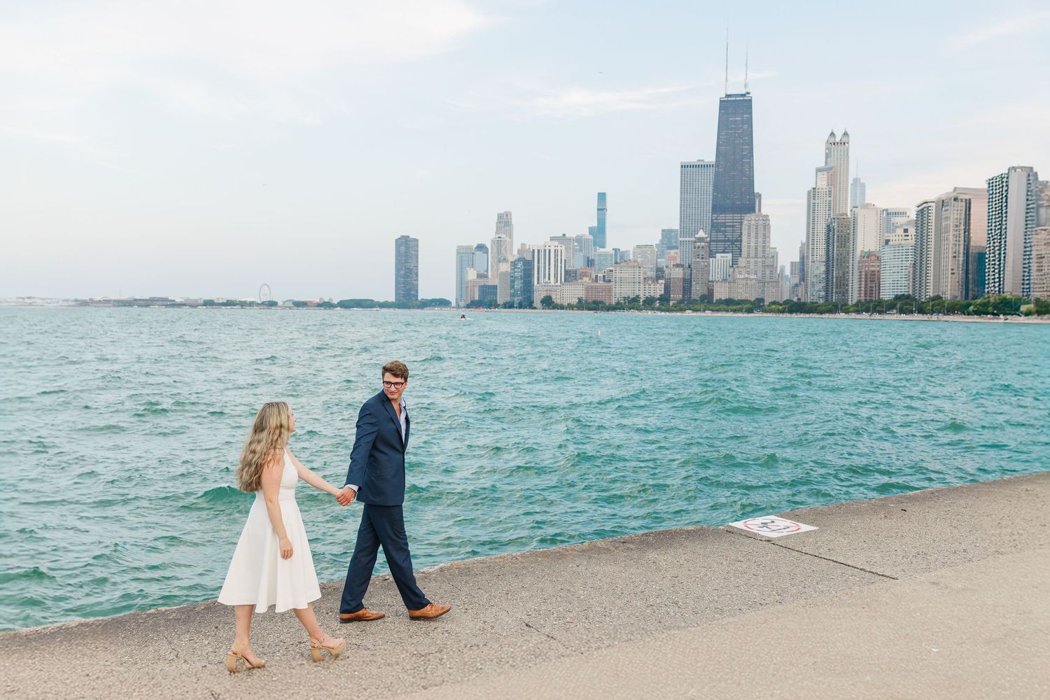 Elizabeth and Joe holding hands with the Chicago skyline in the background at North Avenue Beach during sunset
