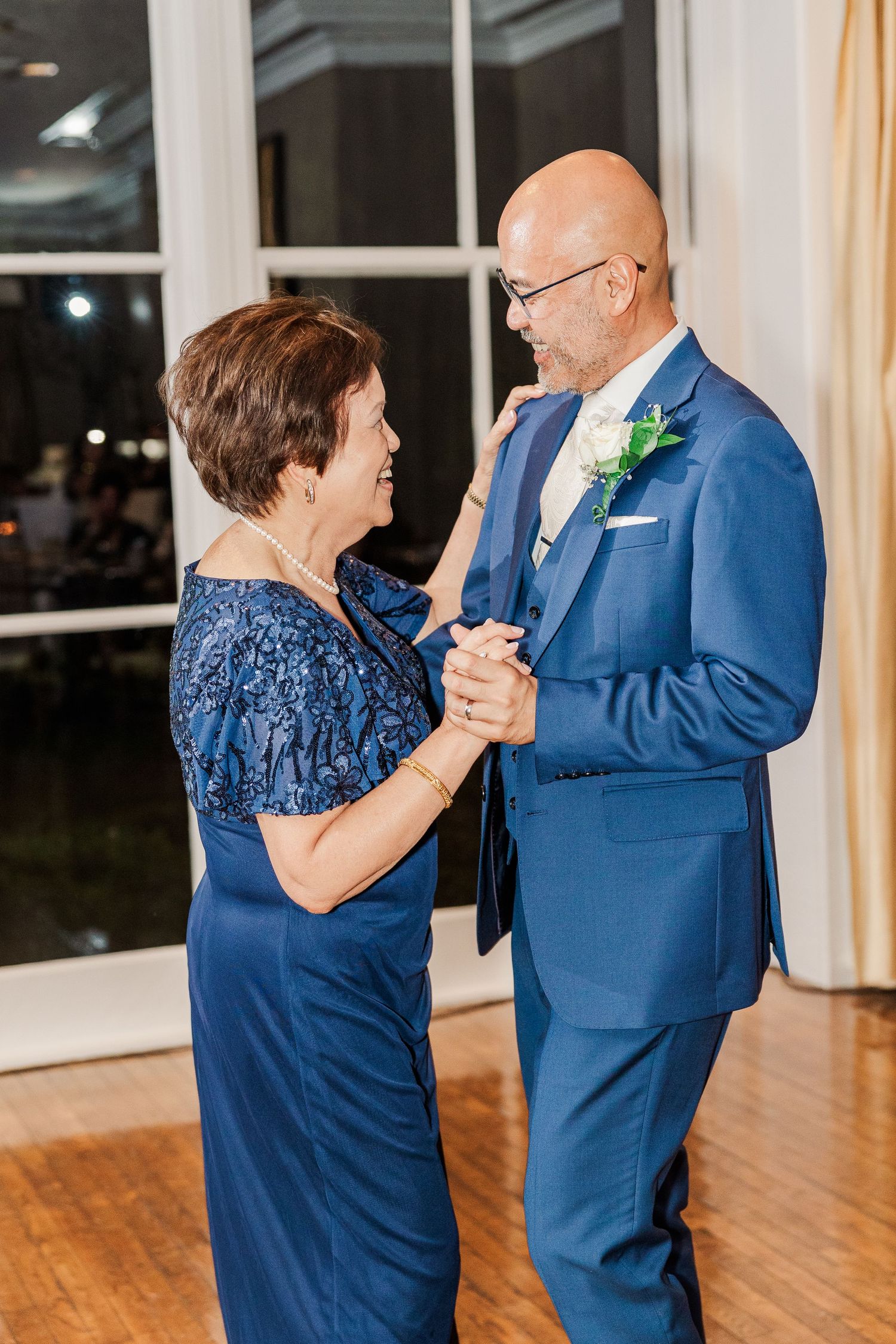 A tender moment shared between two wedding guests dancing in formal attire on a wooden dance floor.