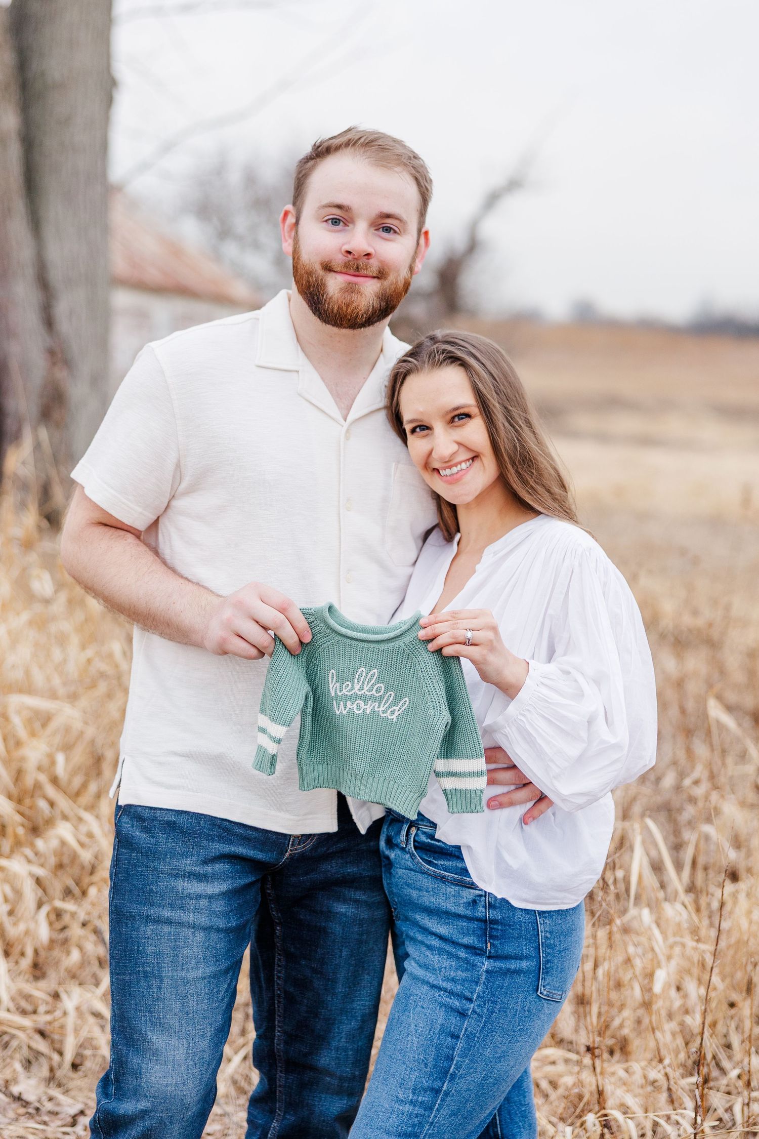 Couple holding baby sweater during pregnancy announcement photos at Sands Main Street Prairie in Cary, Illinois