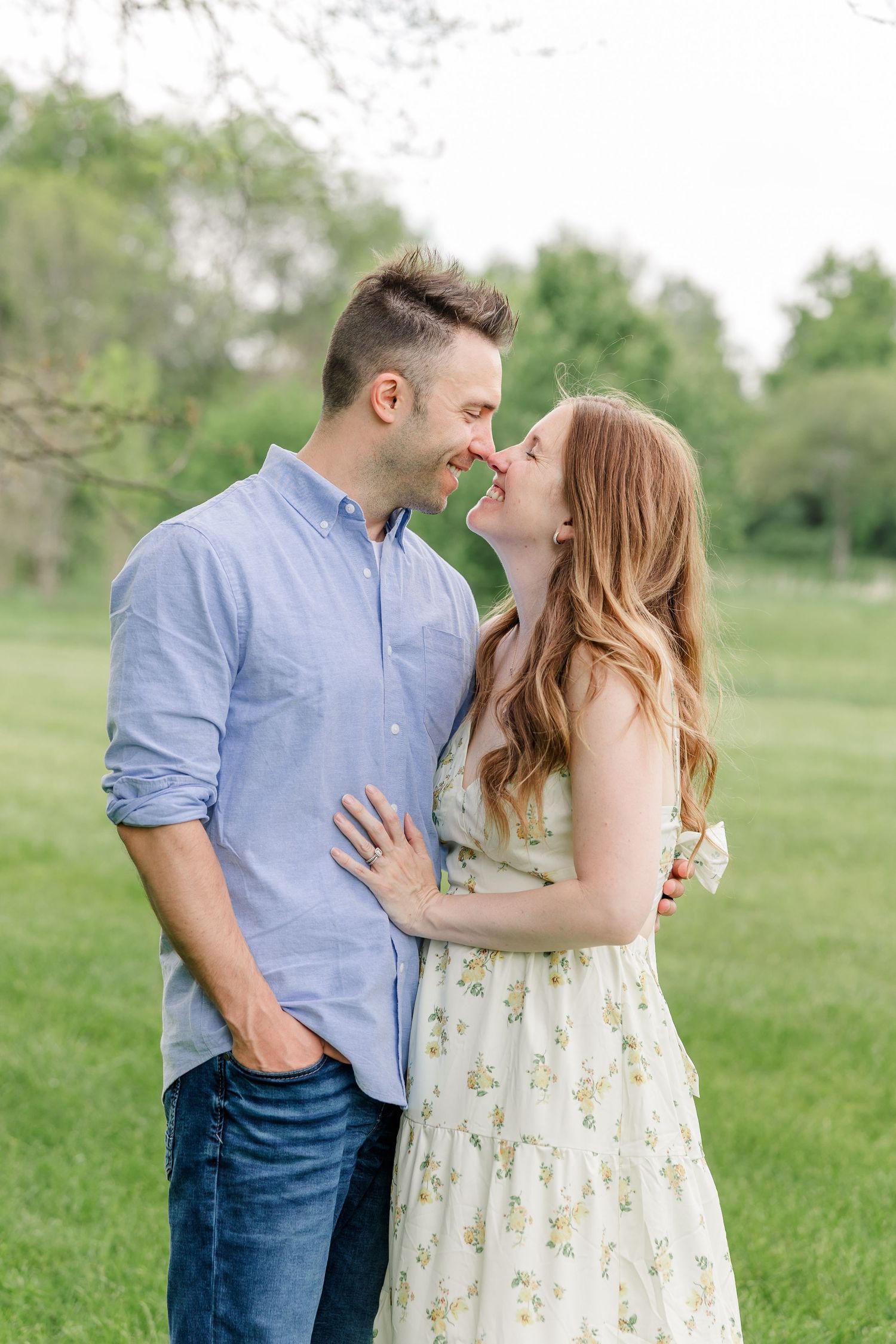 Smiling couple nearly kissing while embracing outdoors in a green park setting during a spring portrait session.