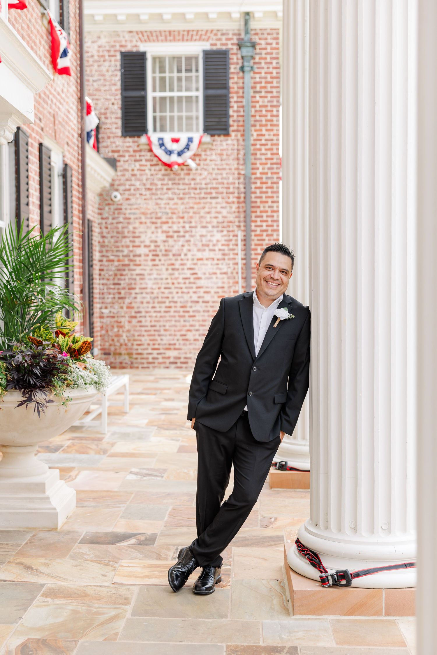 Groom leaning against a white column outside McCormick House during wedding portraits at Cantigny Park.