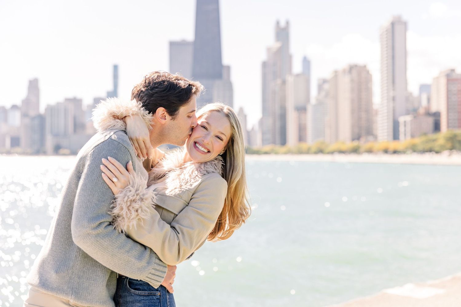 Happy couple embracing and laughing by Lake Michigan with Chicago skyline in background.
