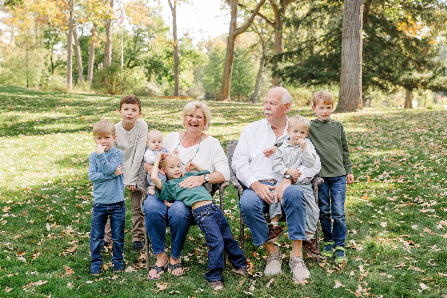Grandparents sitting outdoors with six grandchildren of various ages in an autumn park setting.