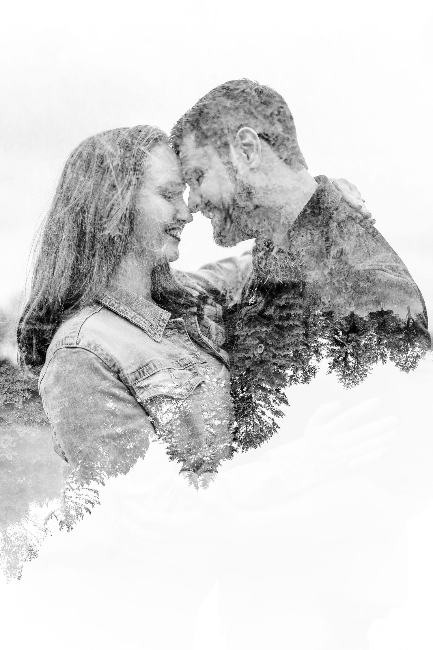 Black and white double exposure portrait of a couple touching foreheads and smiling, blended with a silhouette of evergreen trees.