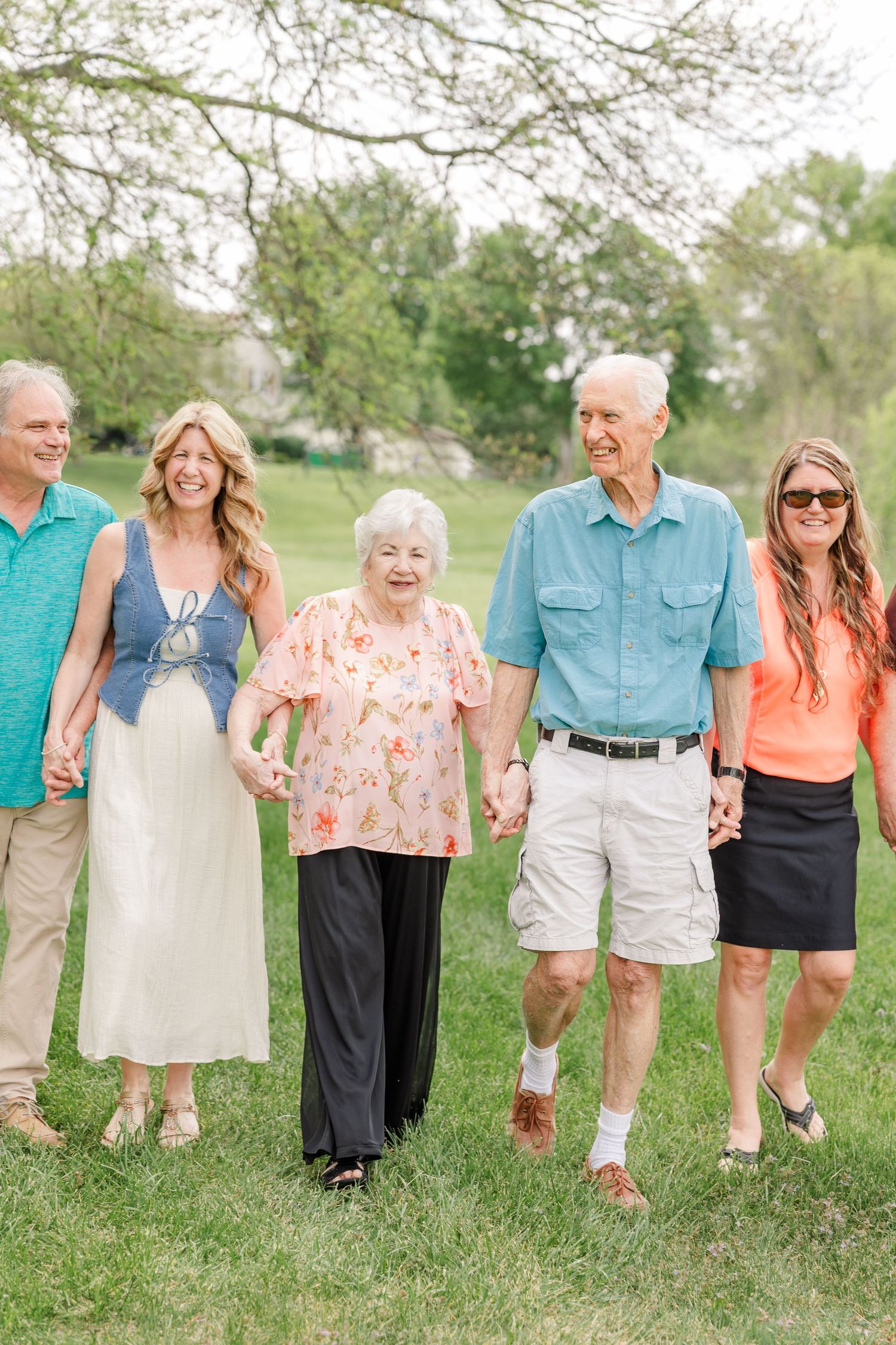 A multigenerational family walks hand in hand together across a green lawn on a sunny spring day.