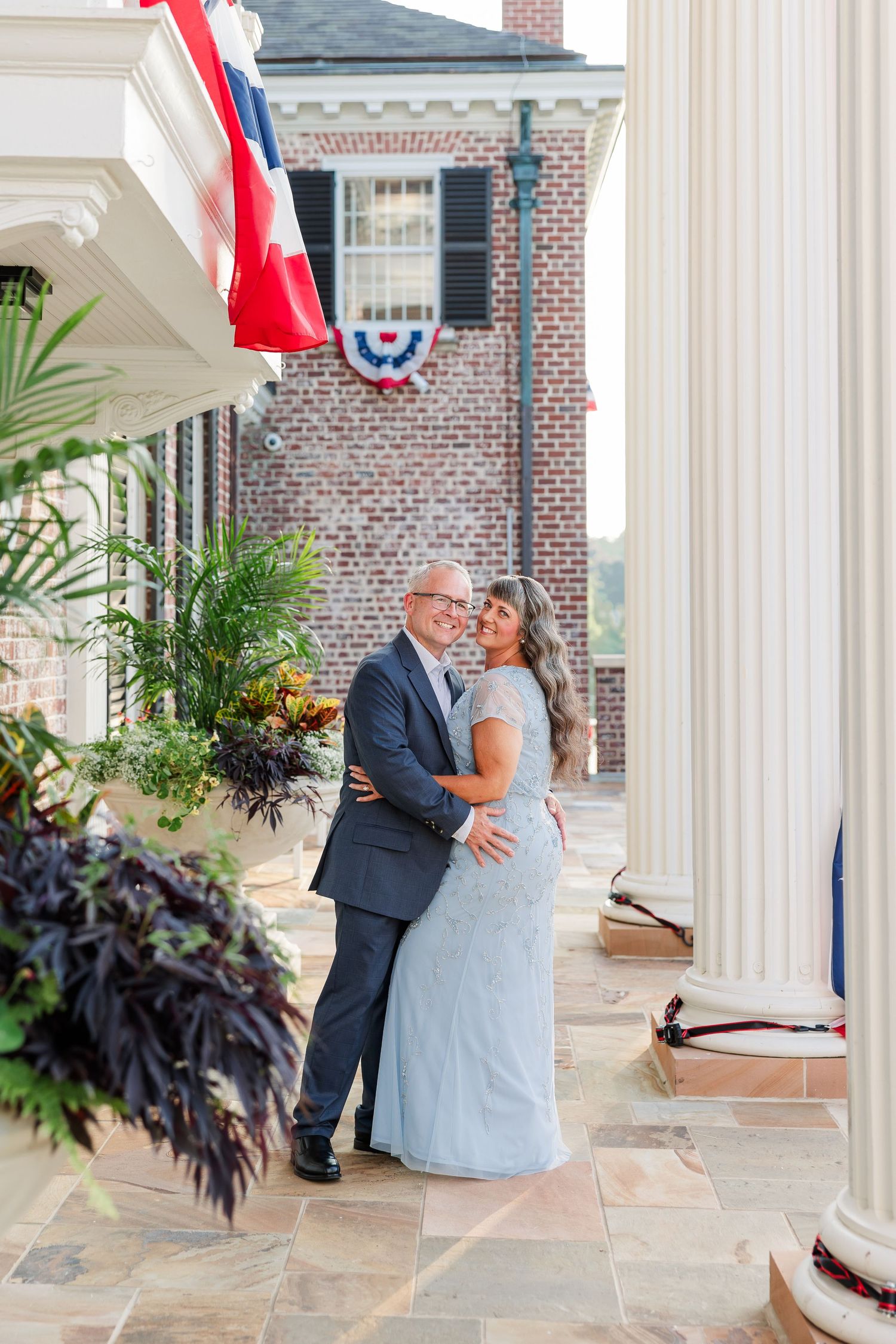 Couple embracing and smiling on a colonial-style porch with patriotic bunting decorations.