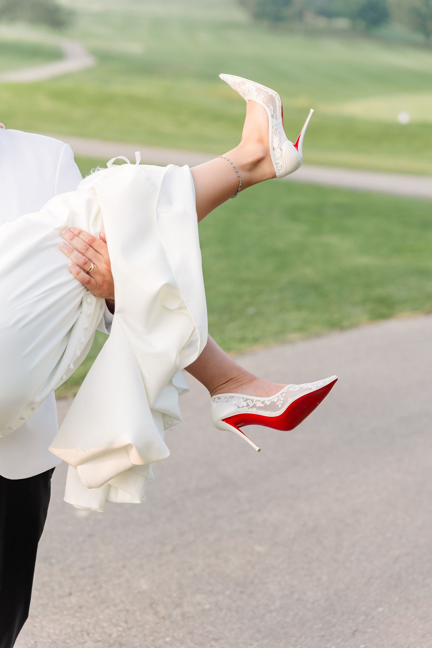 Close-up of bride being carried, showcasing white lace Christian Louboutin red-sole heels.