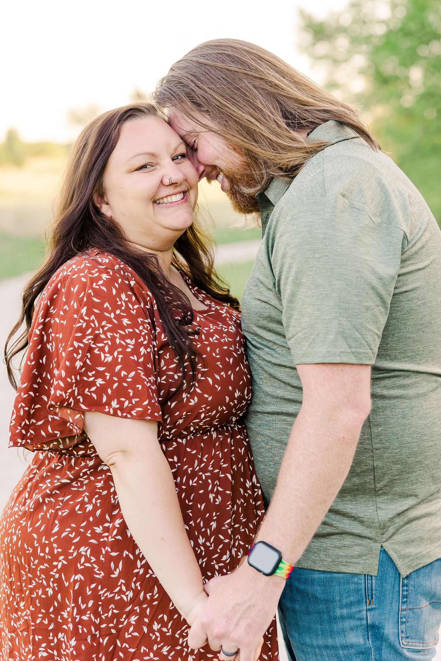 A couple shares an intimate moment while holding hands and touching foreheads outdoors.
