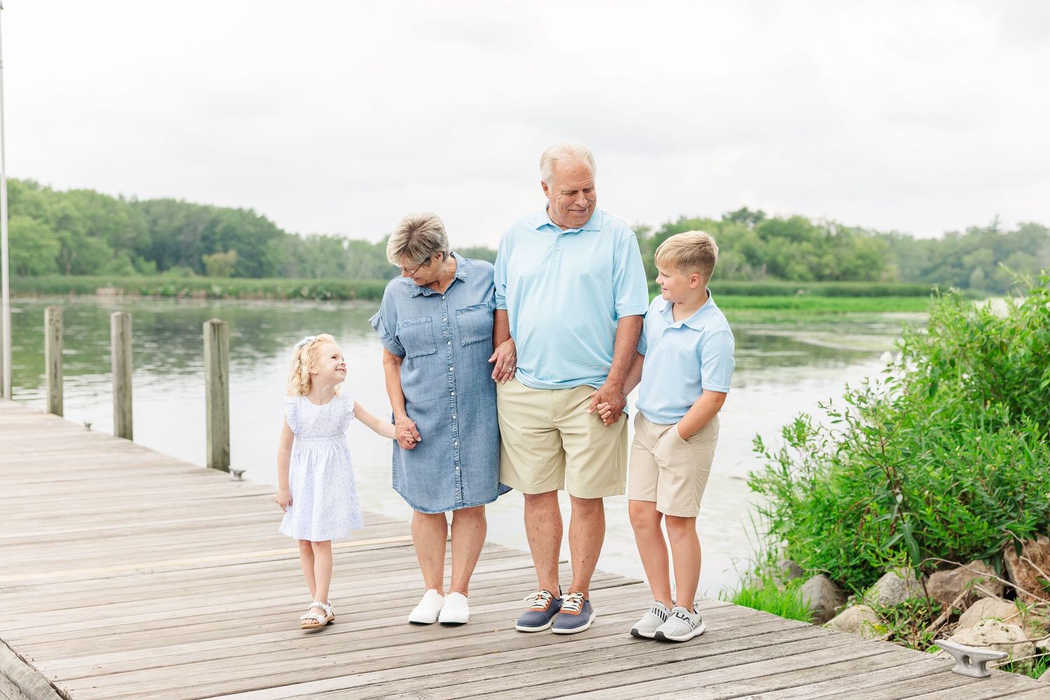 A family walks together along a wooden boardwalk beside a peaceful lake.