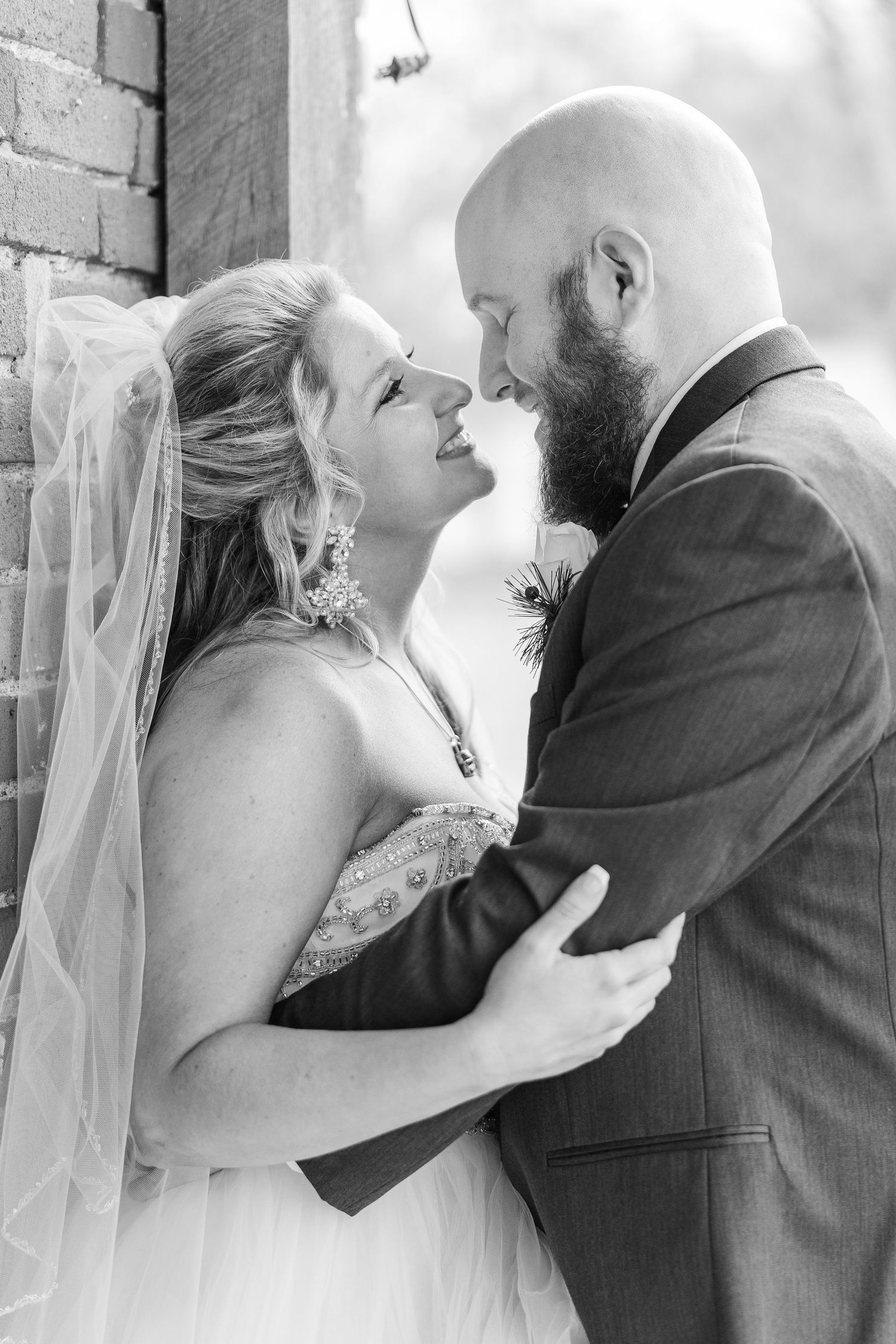 Black and white wedding portrait of a couple sharing an intimate moment by a brick wall.