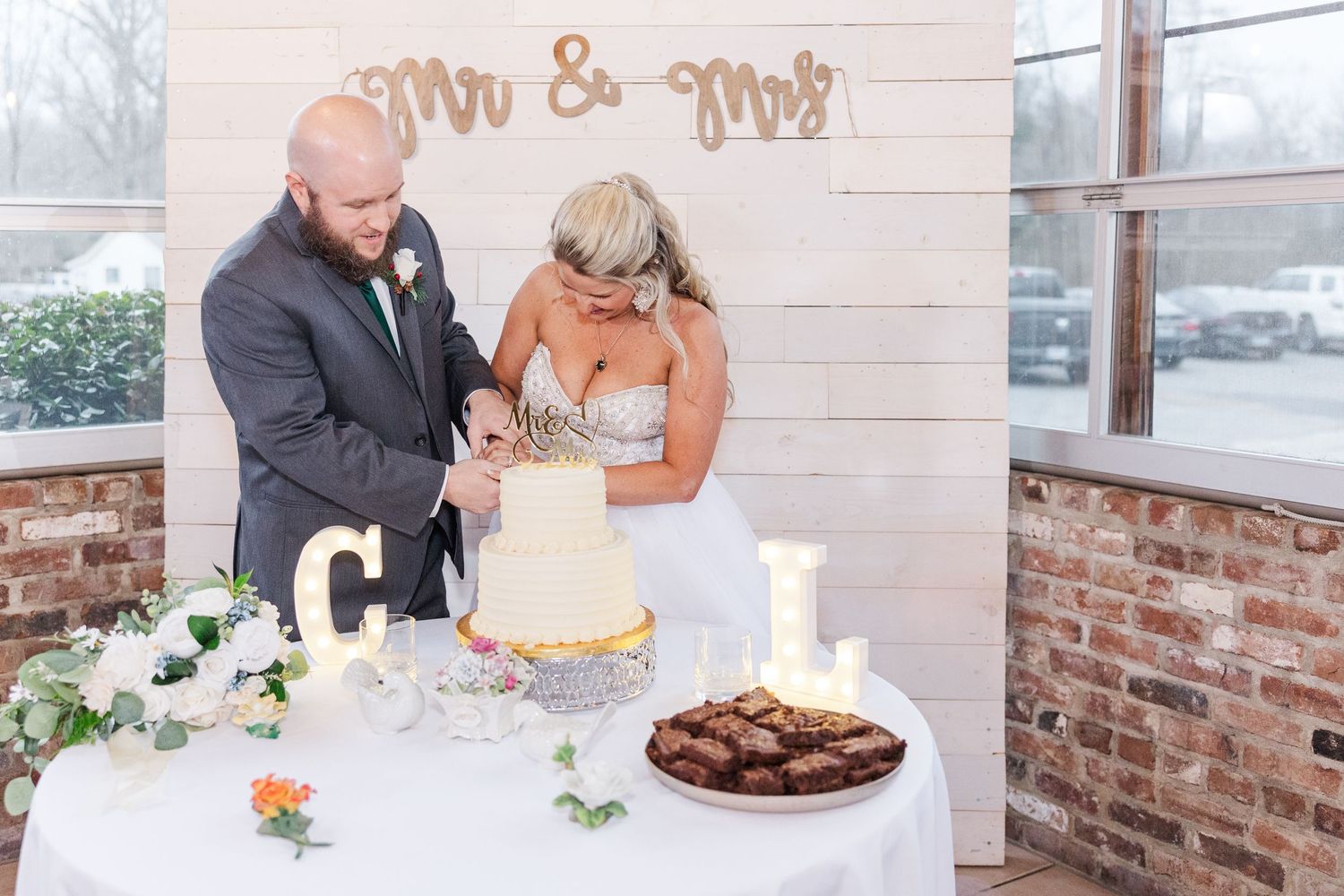 Newlyweds cutting their wedding cake together in front of Mr & Mrs wall sign.