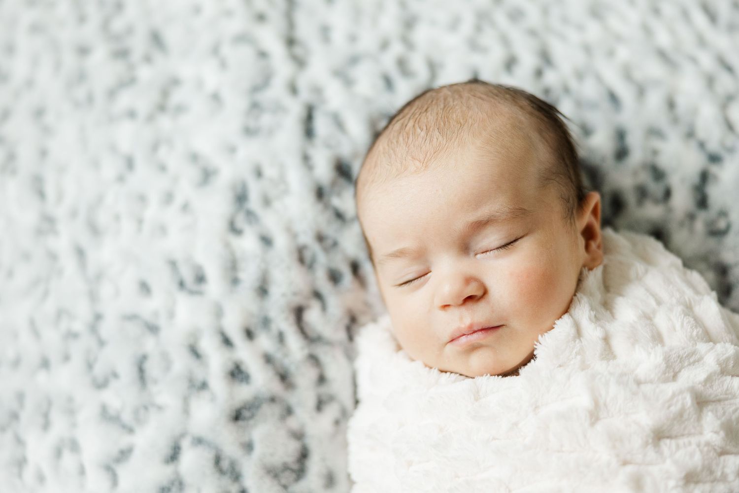 Sleeping newborn wrapped in a soft white blanket during an in-home lifestyle newborn session in Palatine Illinois