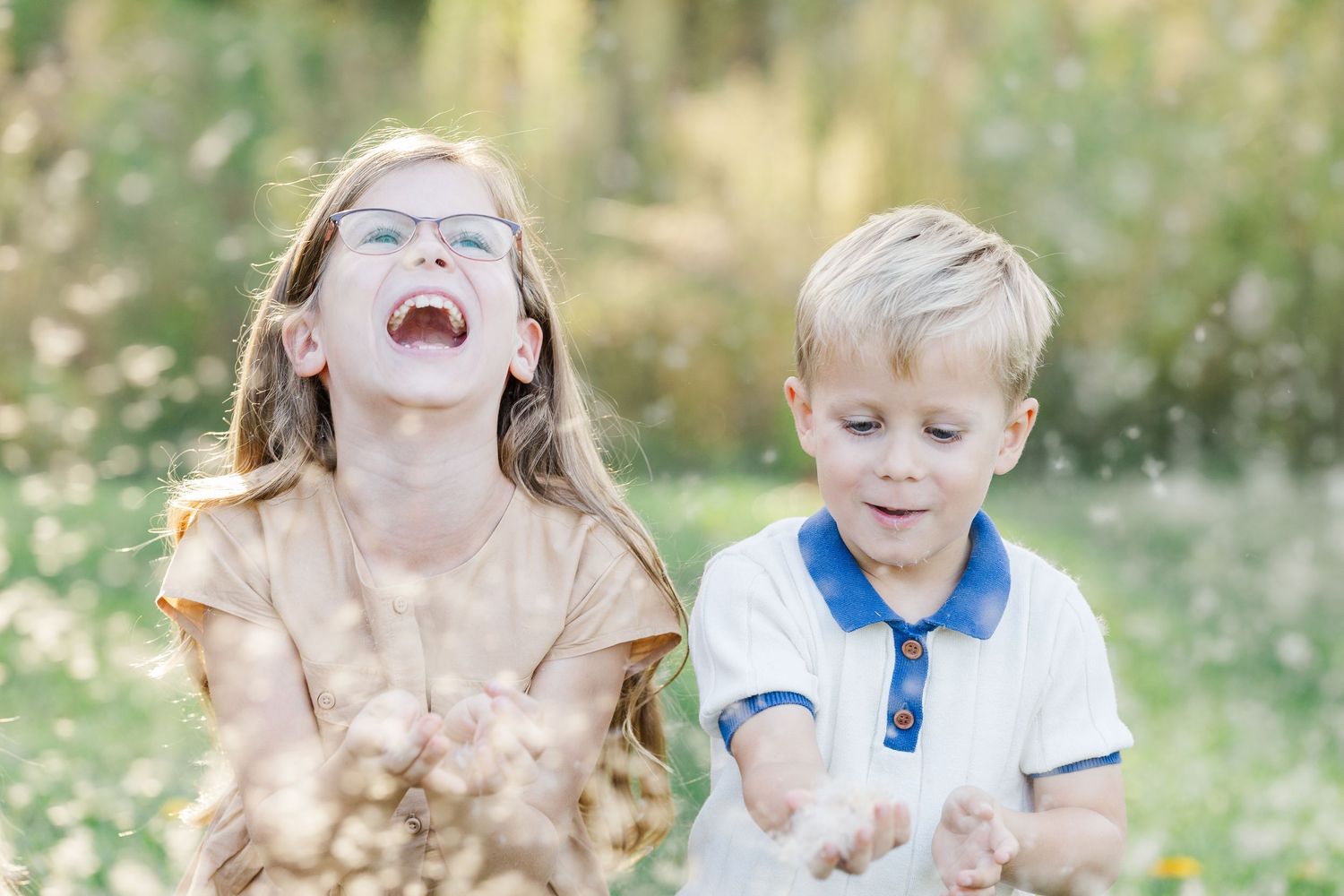 Children play and laugh together while throwing leaves in the air during a sunny autumn day outdoors.