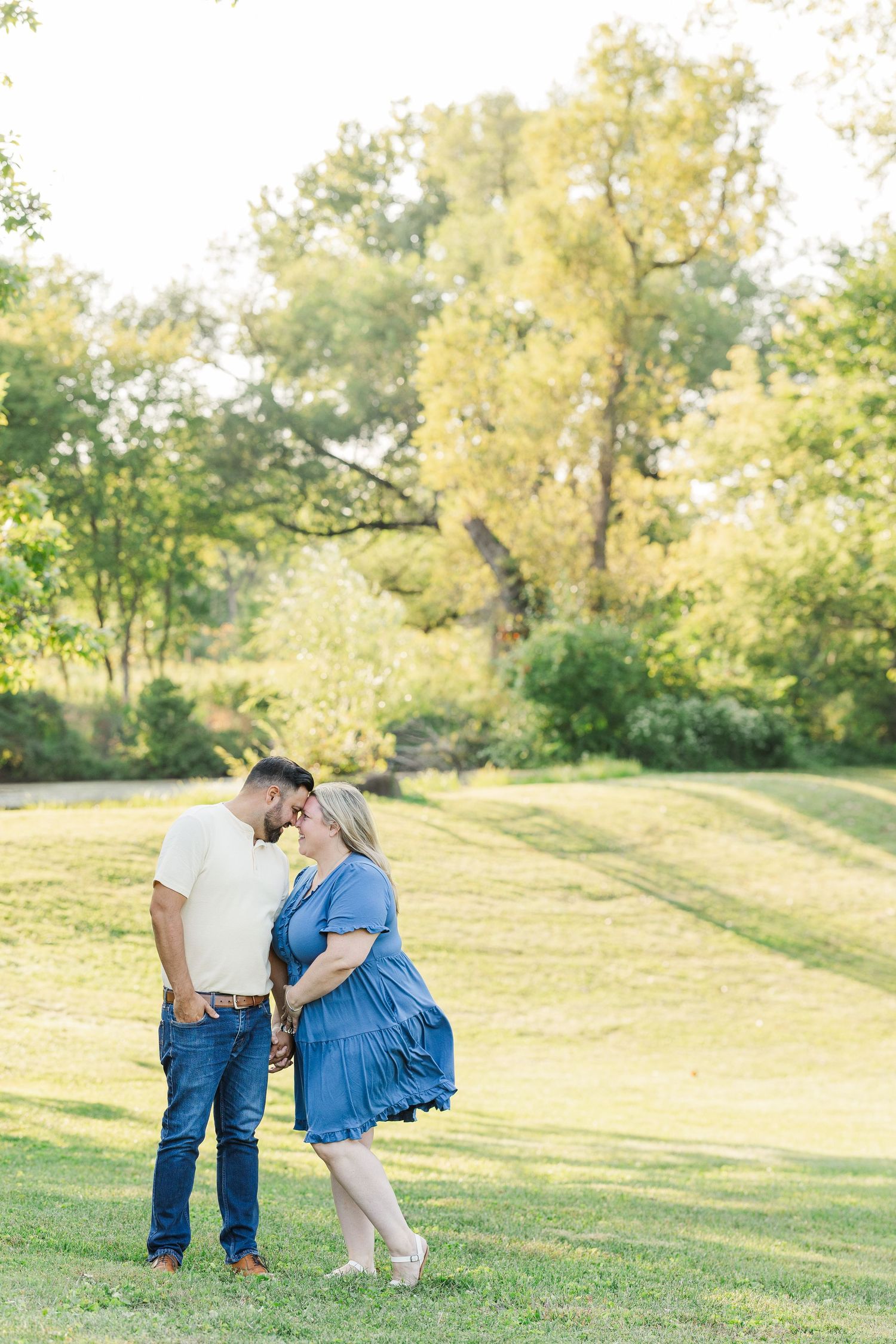 A couple shares a tender moment together in a sunlit grassy field on a summer afternoon.Sorg family portraits at Shamrock Hills Park in Crys
