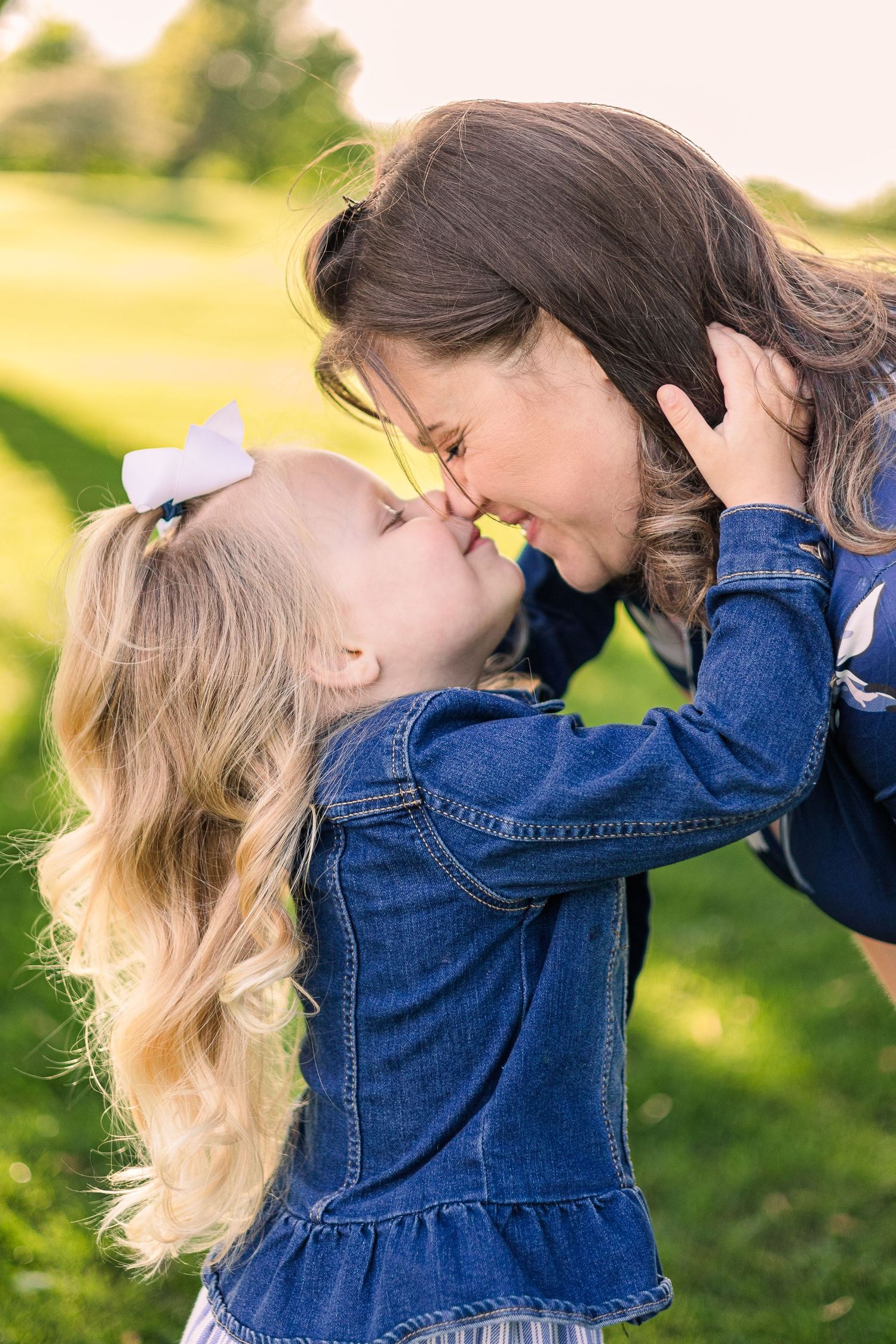 A tender moment captured outdoors showing affection between a young child in denim and an adult in a sunny garden setting.