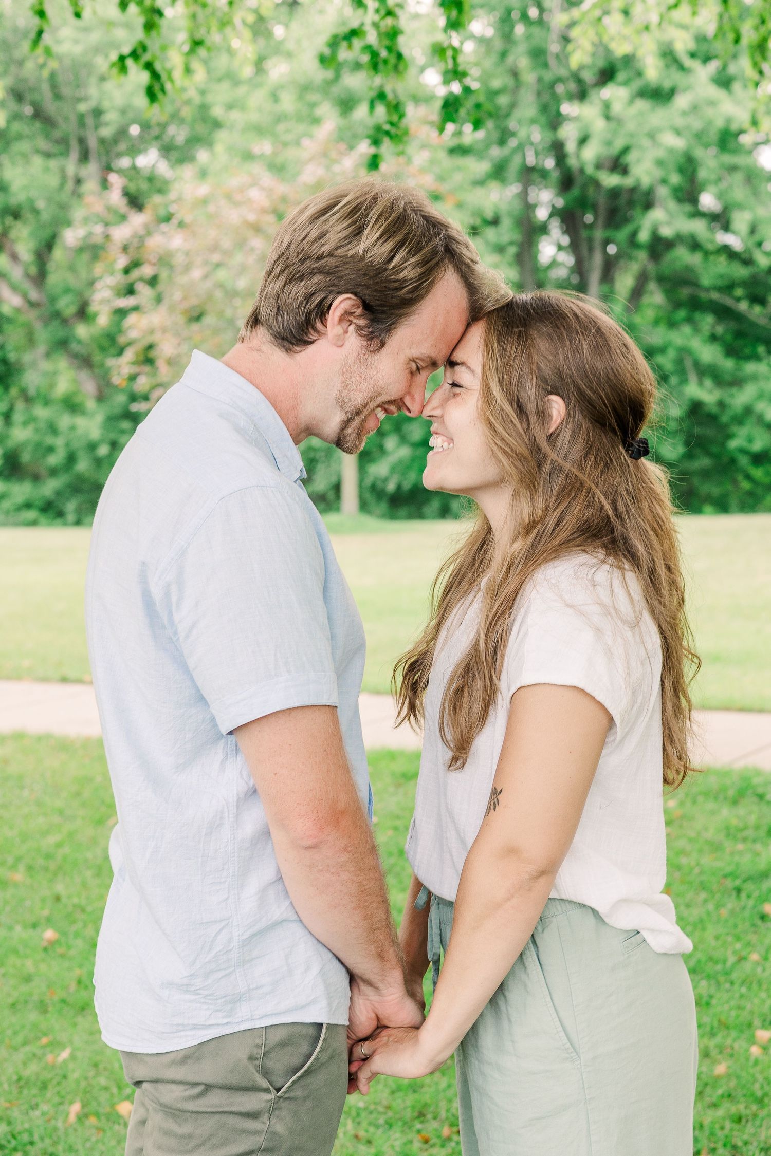 A romantic couple shares an intimate moment outdoors in a lush green park setting.