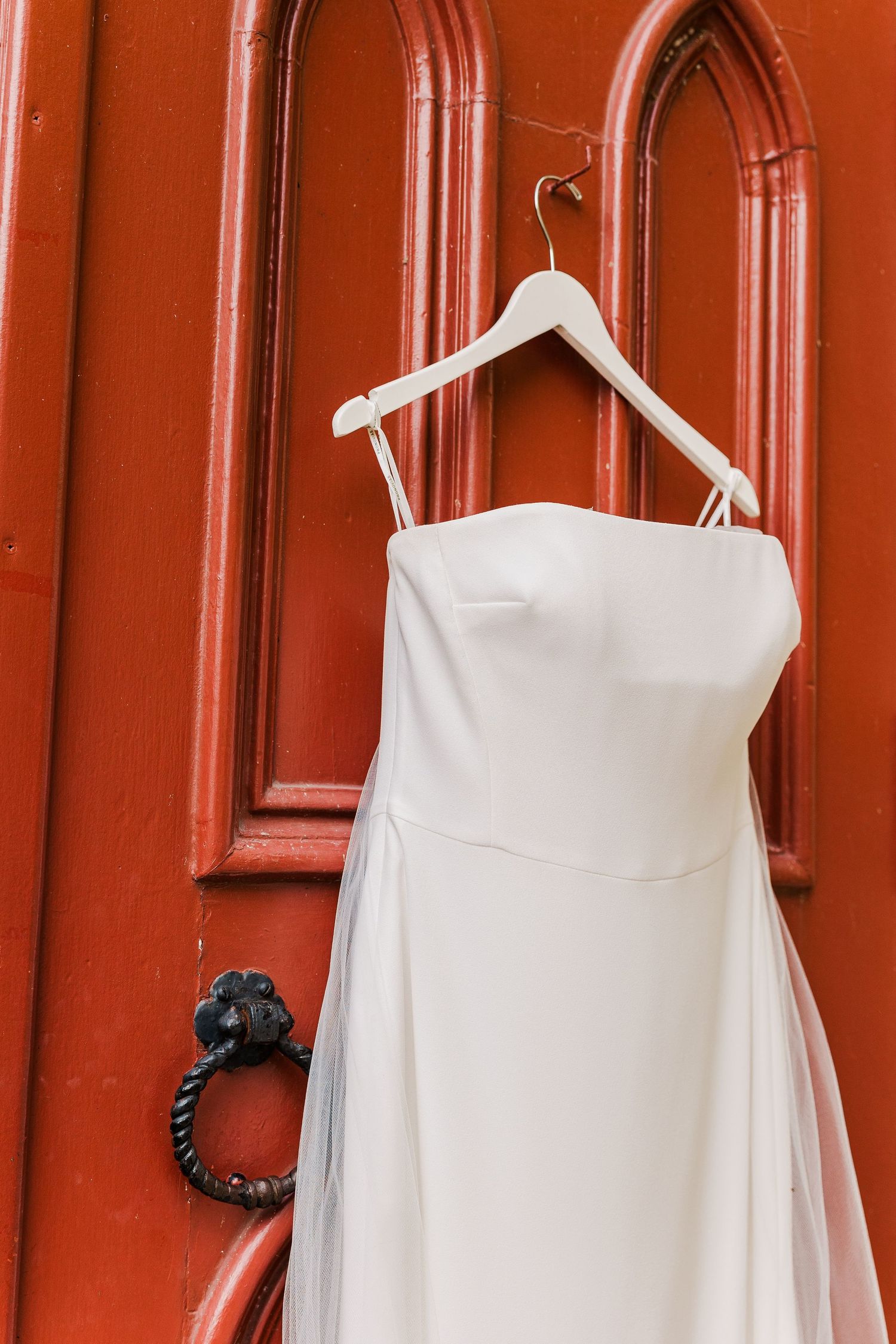 Elegant white wedding dress displayed against a bright red door with vintage hardware.