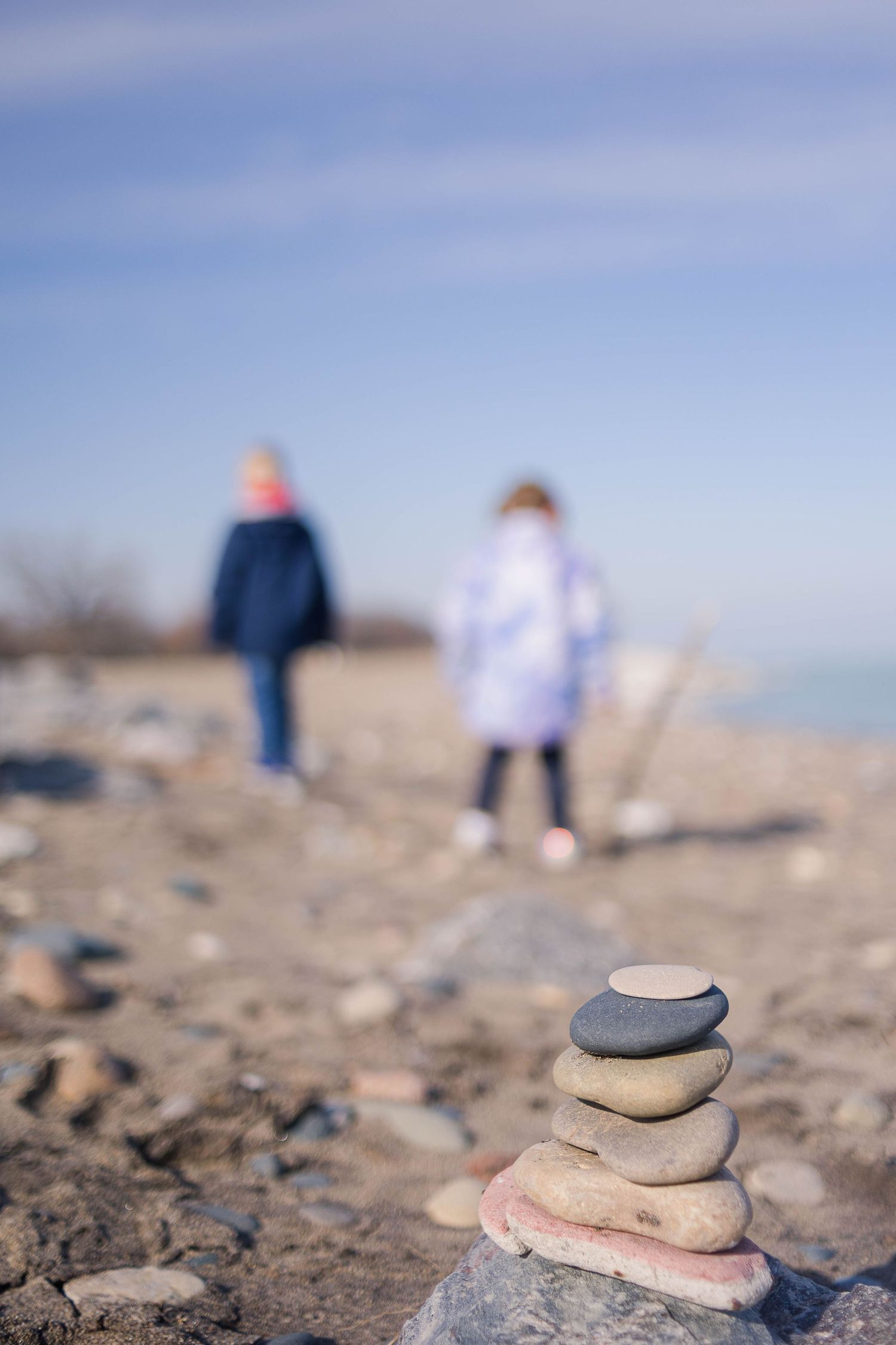 Balanced rock stack on beach with soft focus figures walking in distance.