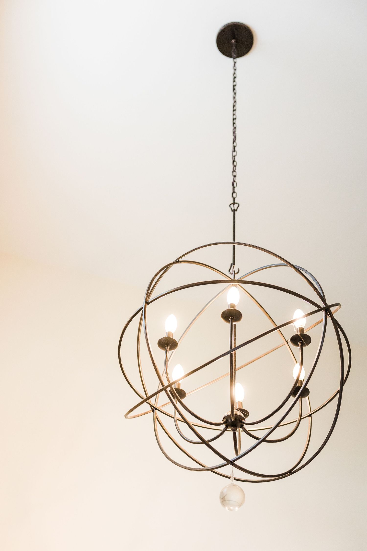 Modern spherical chandelier with orbital metal rings and exposed bulbs hanging from ceiling.