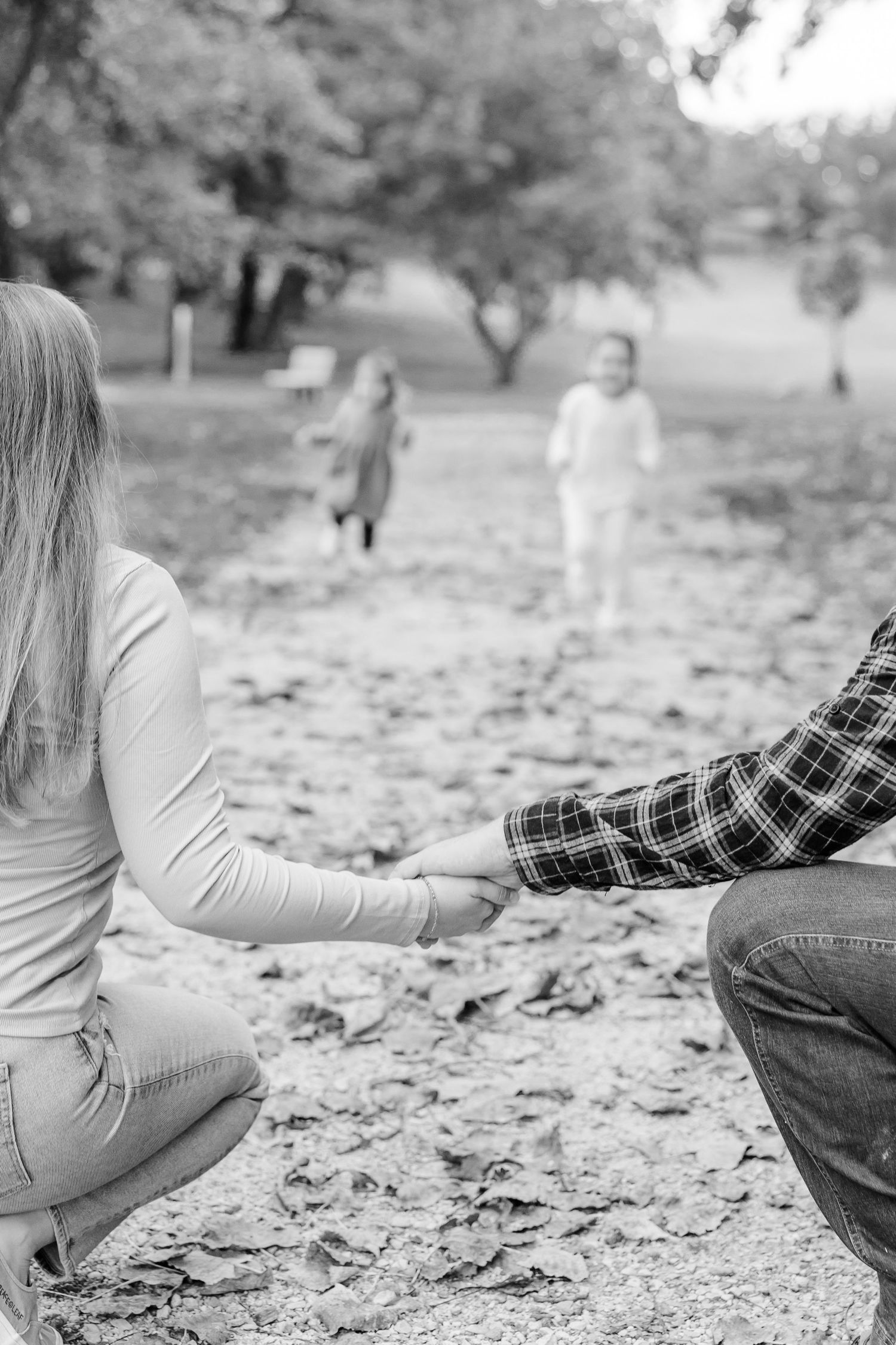 Black and white photo of a couple holding hands as two children run toward them in a leaf-covered park.