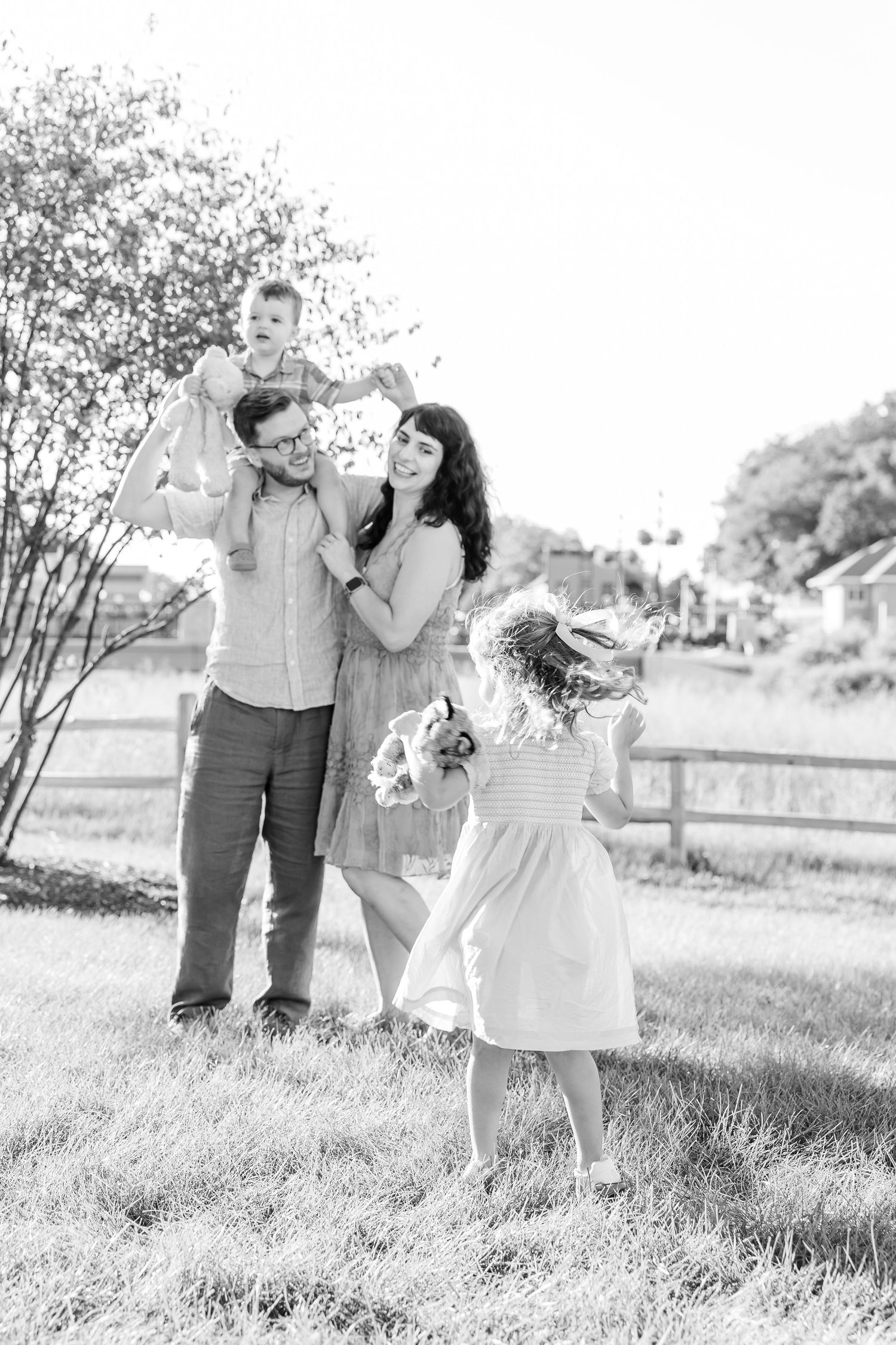 Black and white family photo with parents and two young children playing outdoors near a wooden fence.