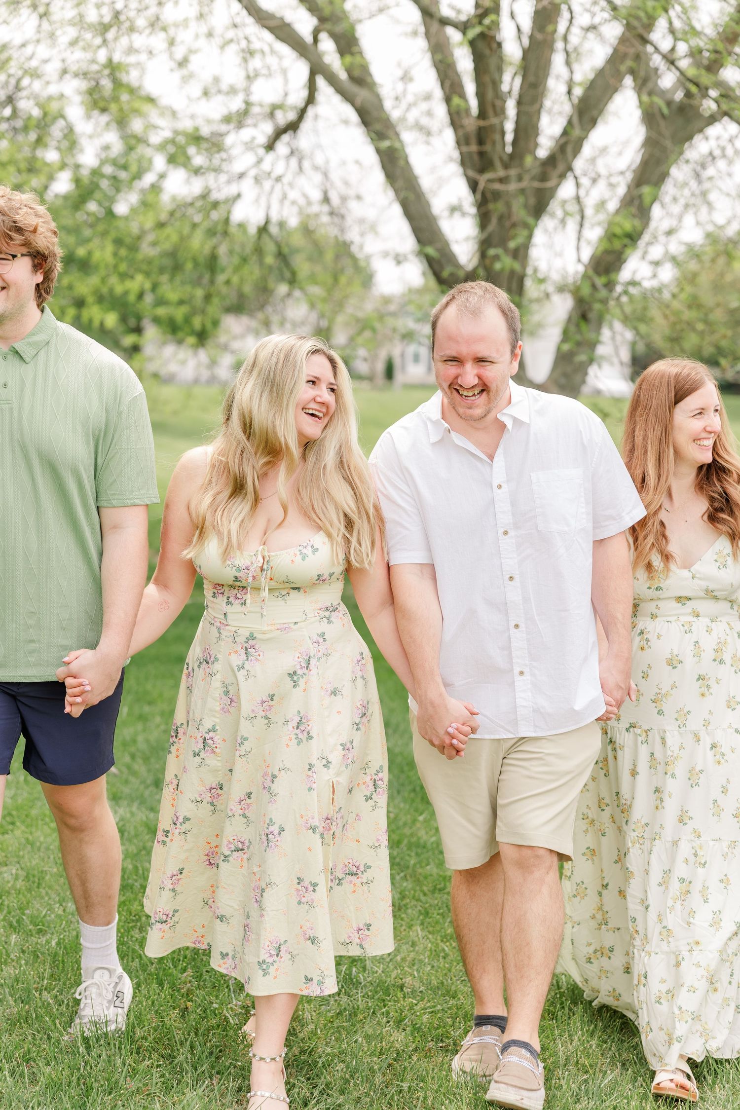 Happy family of four walking hand in hand through a lush green park laughing together on a bright day.