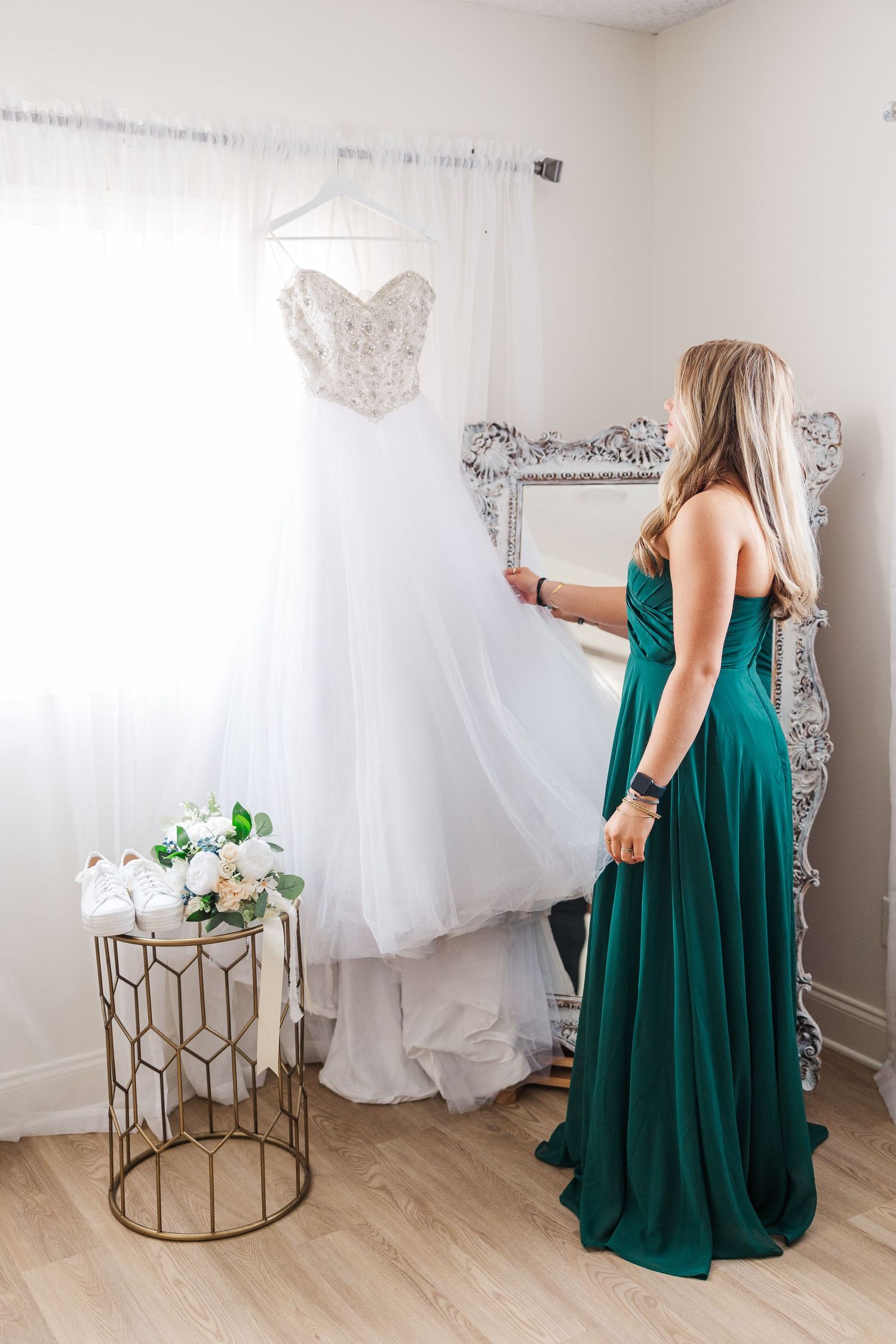 A green-dressed figure admiring a white wedding gown displayed on a hanger near a decorative table.