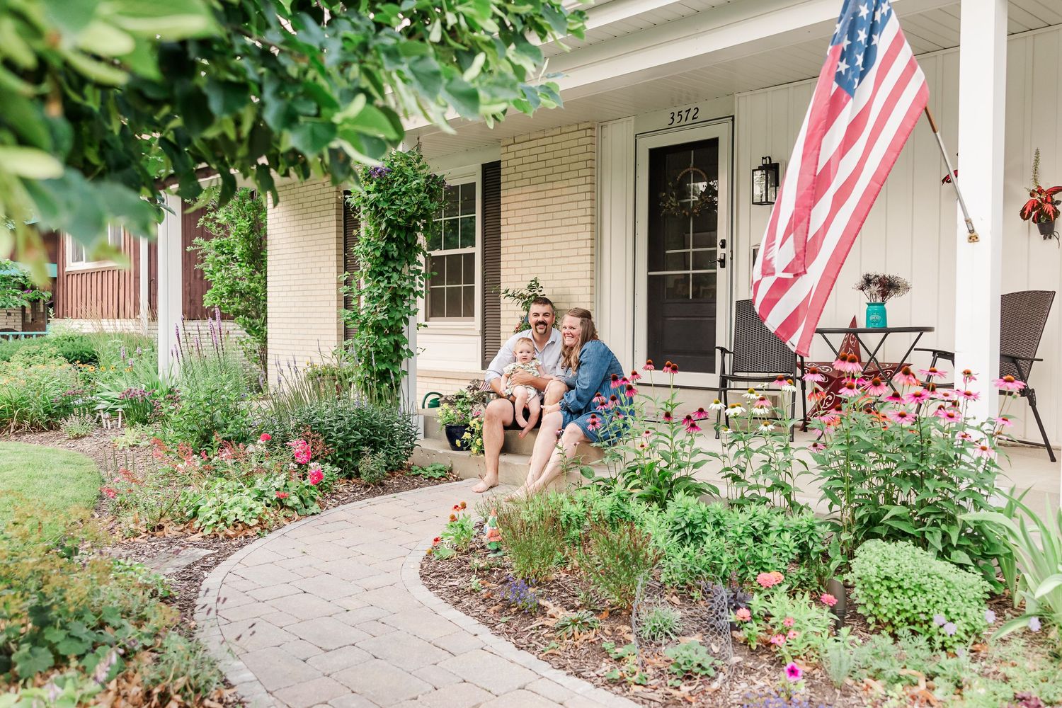 A charming home entrance with American flag and curved garden path lined with flowers.