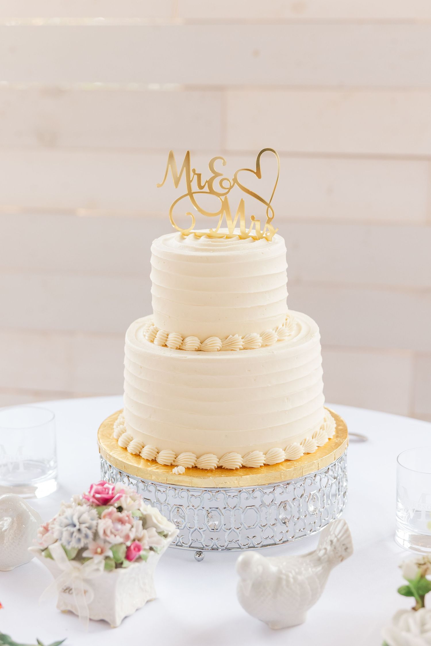 Elegant two-tier white buttercream wedding cake with gold Mr & Mrs topper.