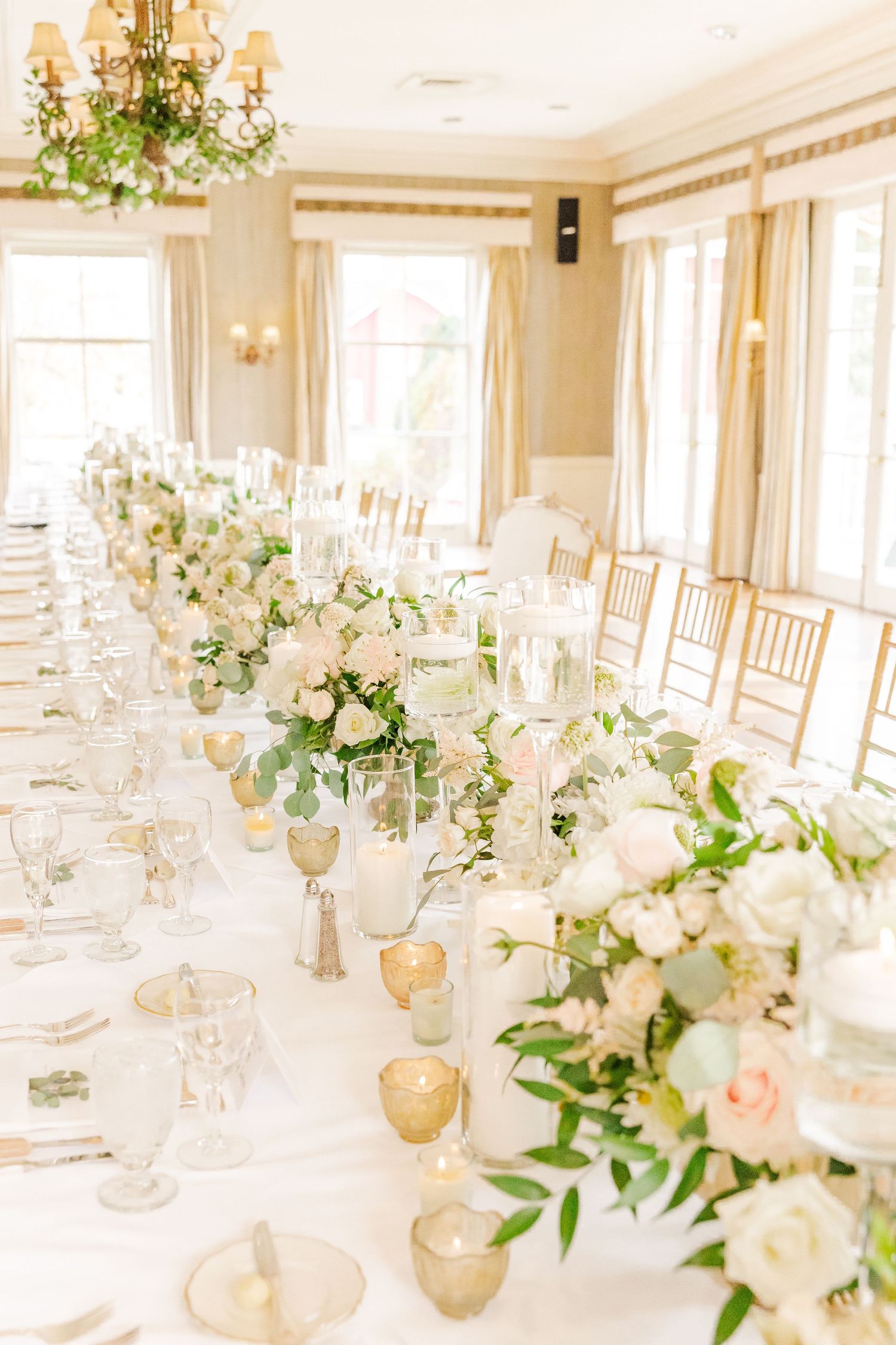 Bright wedding reception room with long tables decorated in white and blush floral arrangements.
