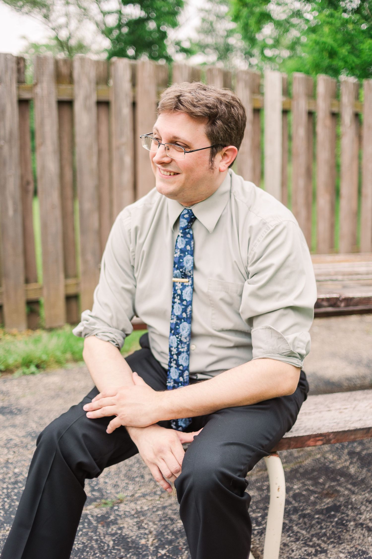Person in business attire sitting on bench by wooden fence.