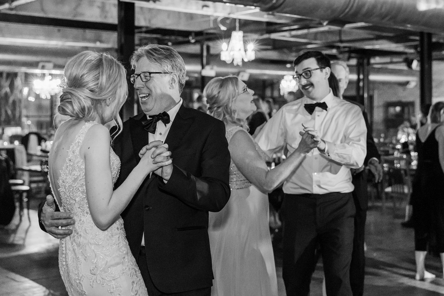 Couples slow dancing at an elegant wedding reception with ambient lighting.