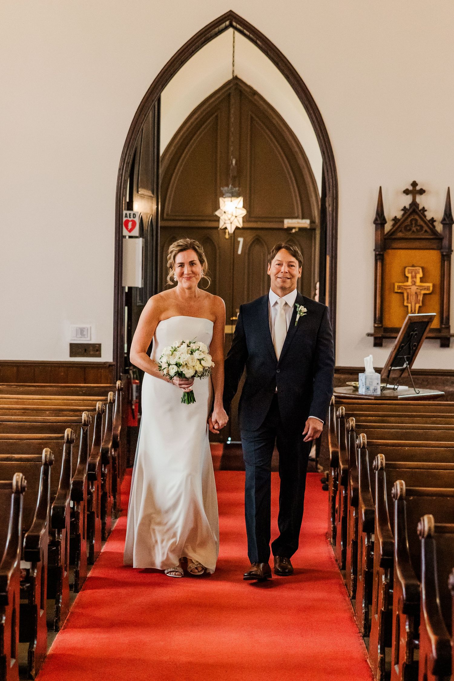 A couple walks down the red-carpeted church aisle together after their wedding ceremony.