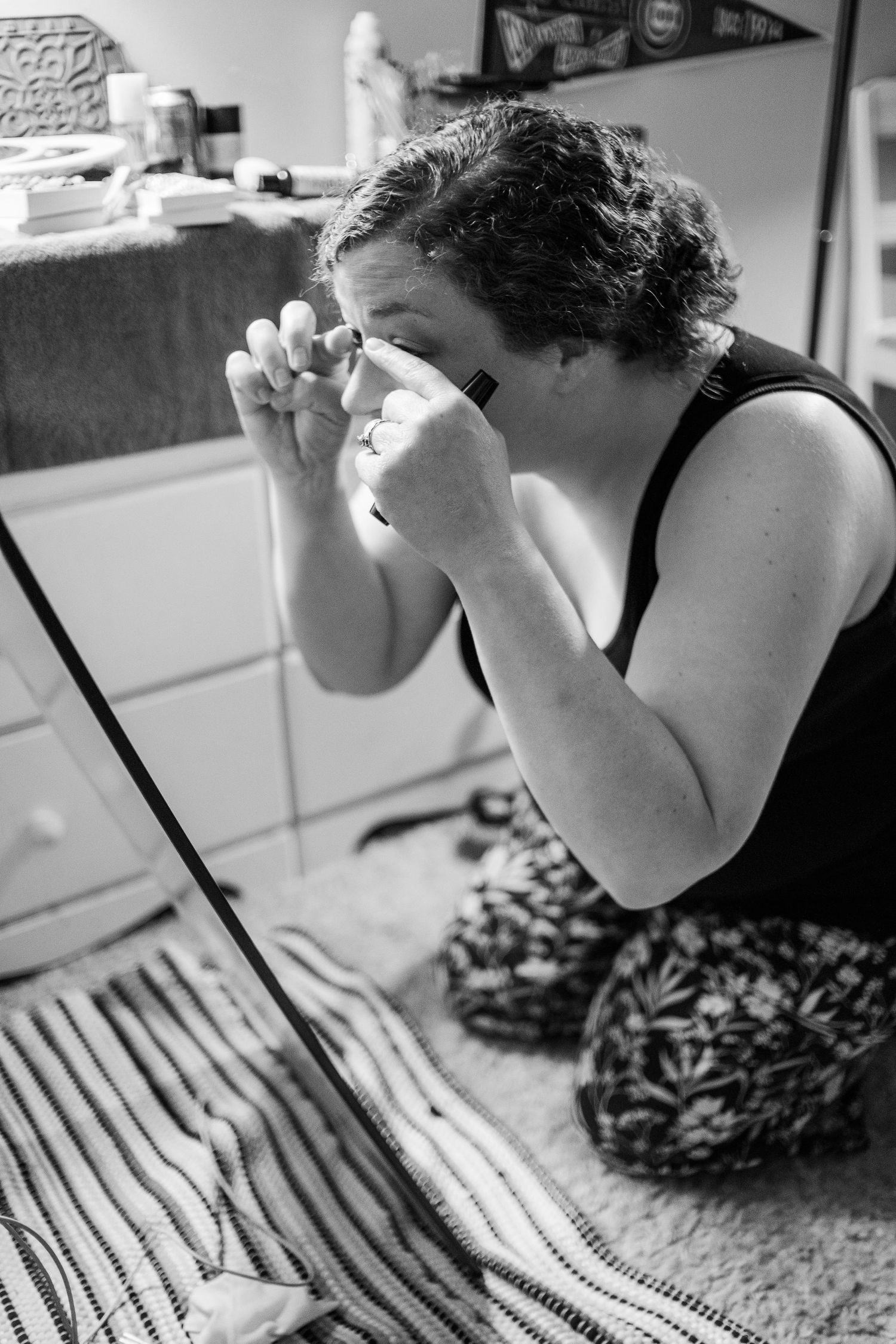 Black and white image of someone applying eye makeup in front of a mirror.