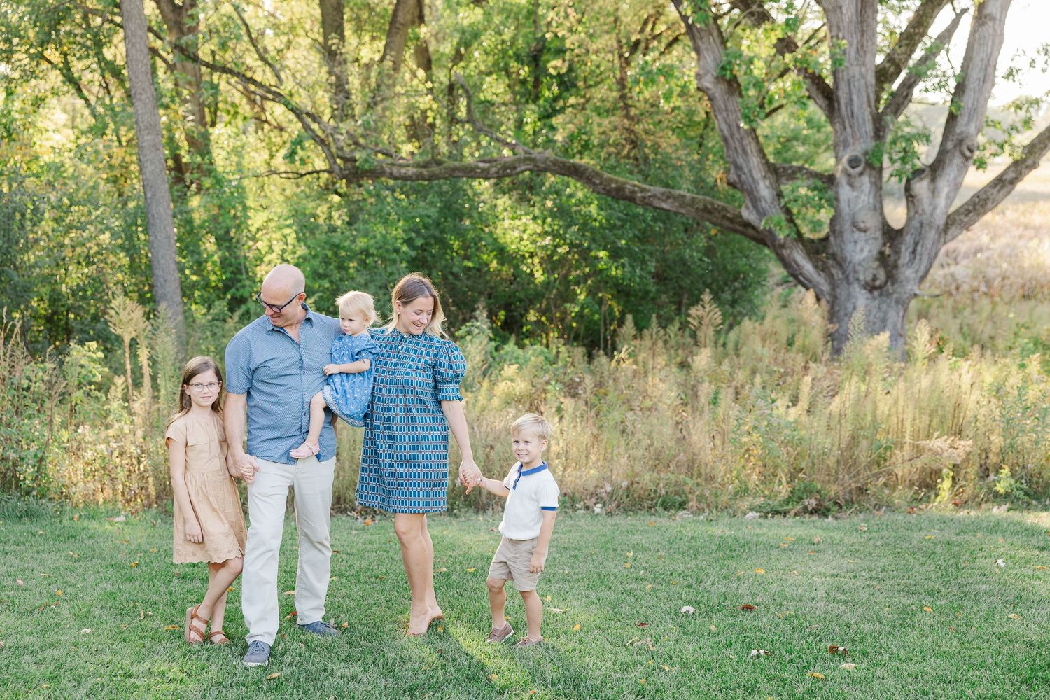 A family walks together through a sunlit grassy field on a warm autumn afternoon.