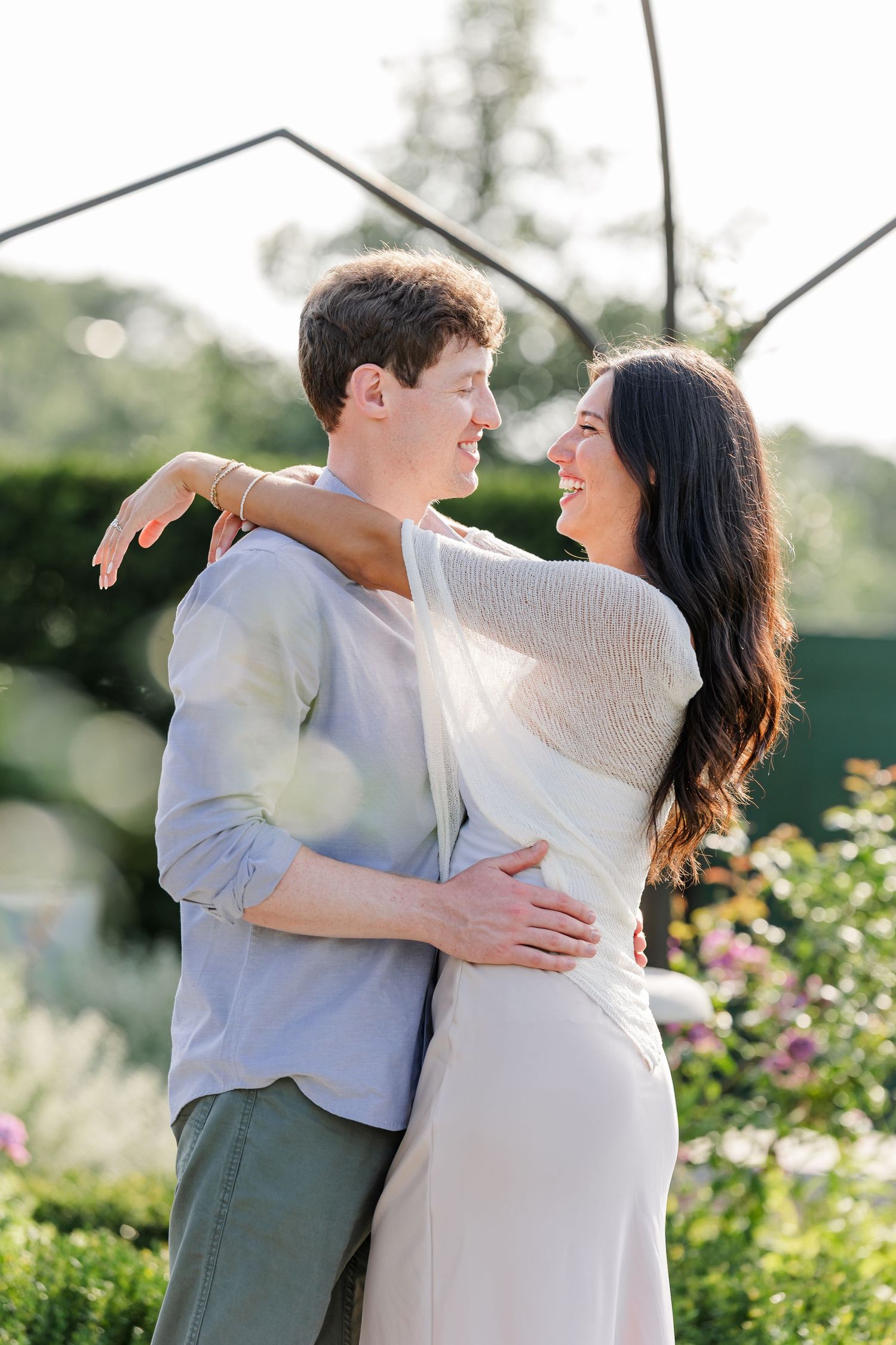 Alysia and Jack smile at each other while embracing in the rose garden.