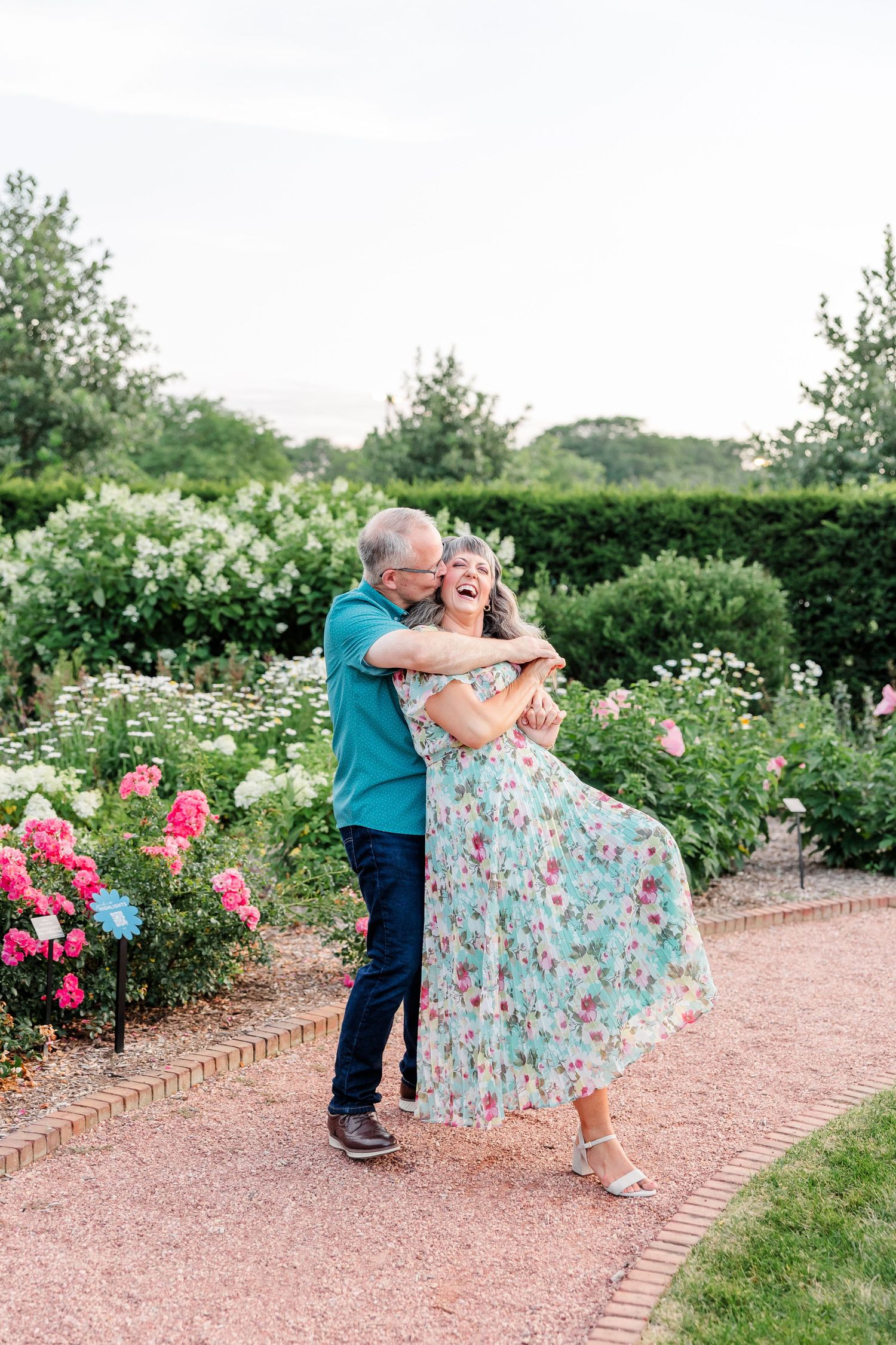 Happy couple embracing and laughing in a lush garden surrounded by colorful blooming roses.